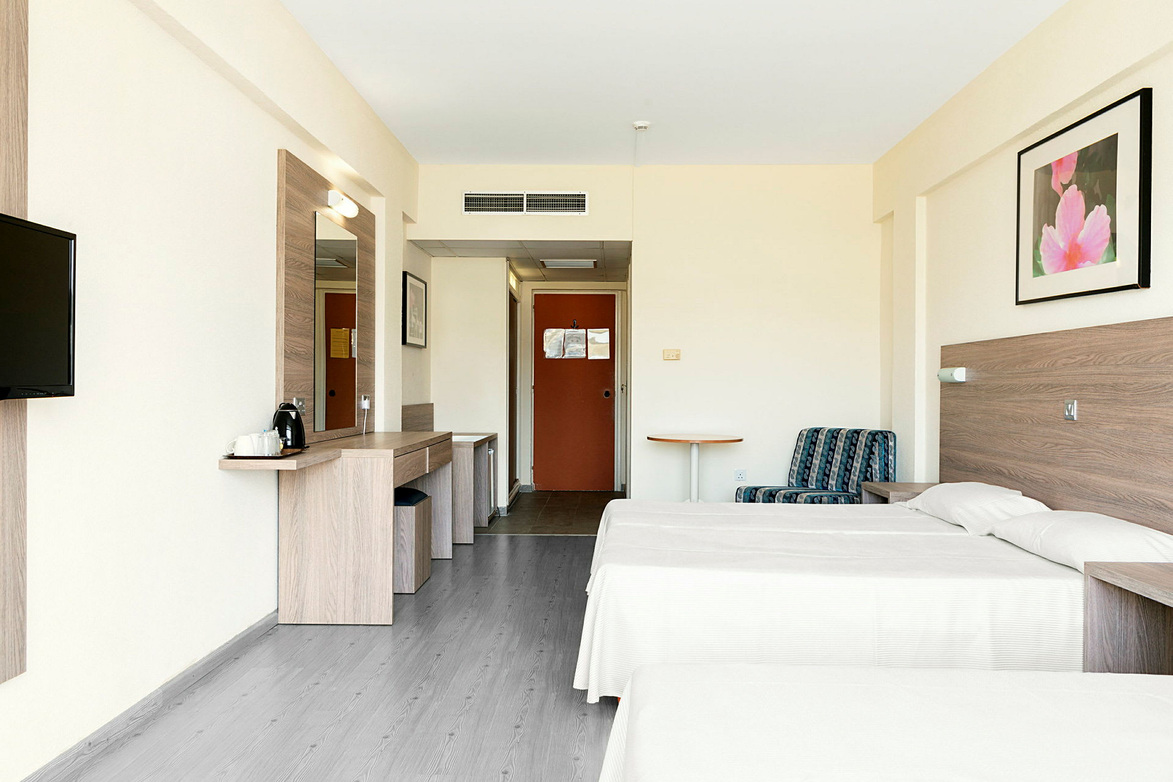 Bildet viser et hotellrom med to enkeltsenger, en sitteplass og et skrivebord. (AI-generert tekst)