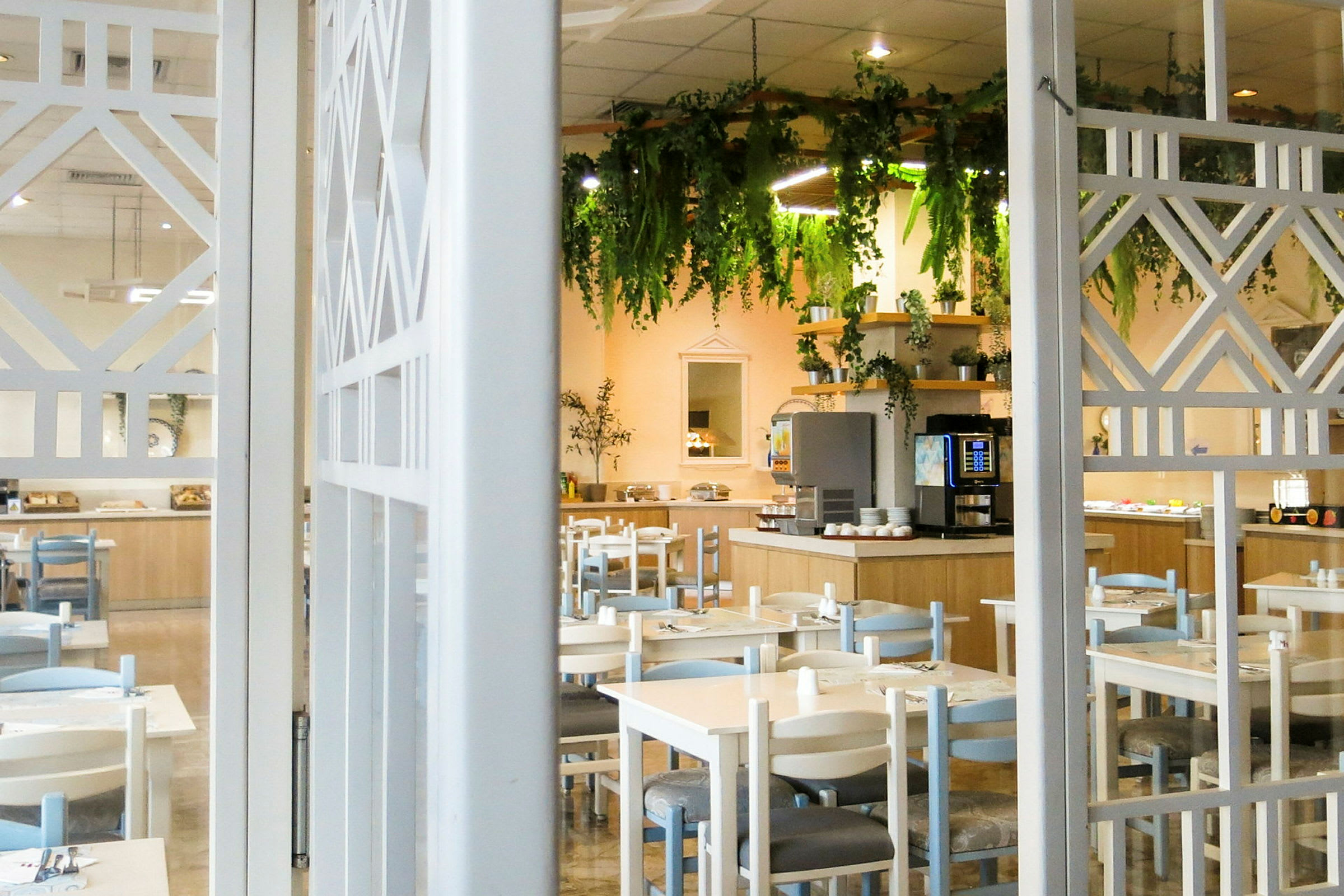 En restaurant med bord og stoler, samt en dekorert buffet og hengende grønt. (AI-generert tekst)