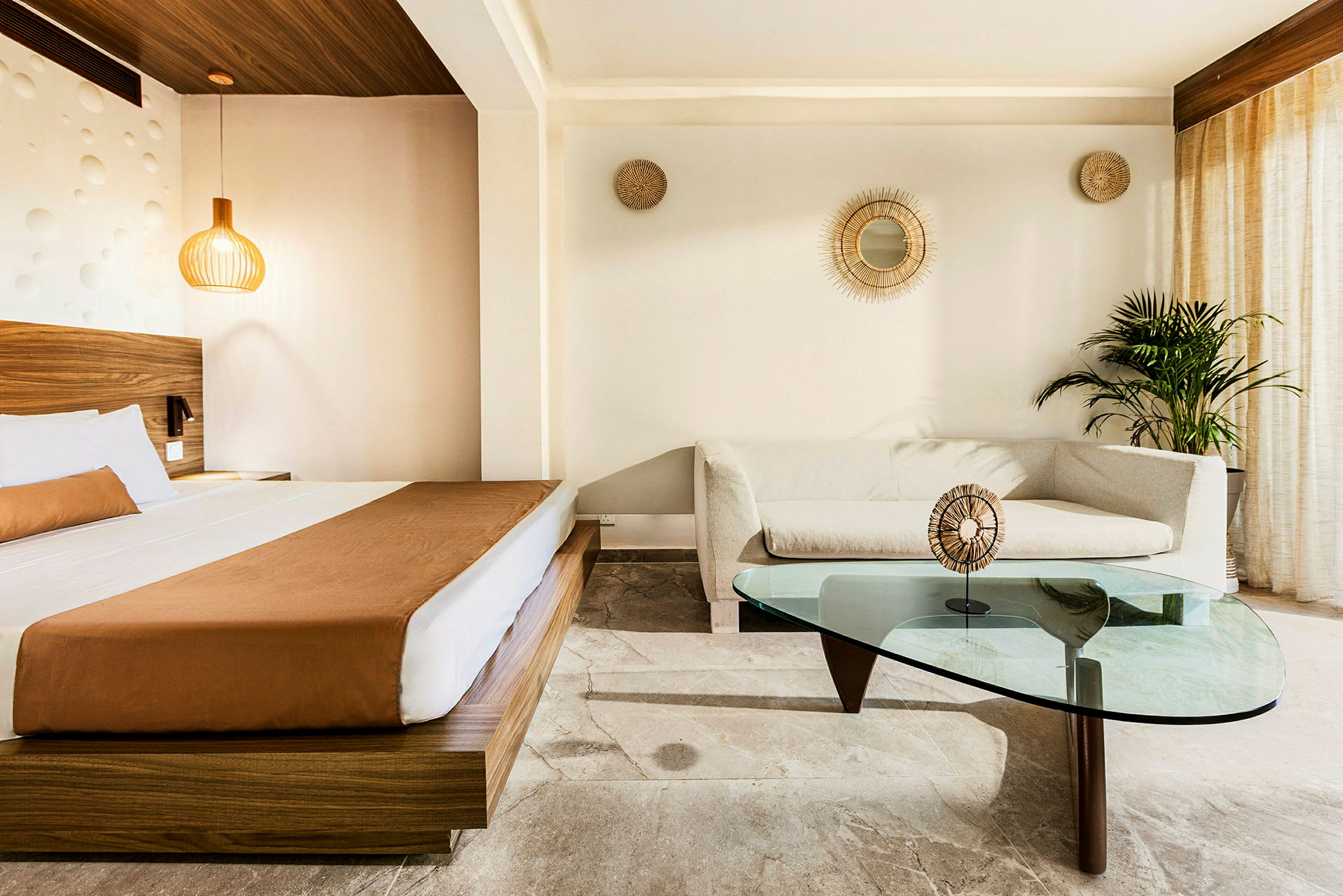 En moderne hotellsuite med en seng, en sofa og et glassbord foran lyse vegger. (AI-generert tekst)