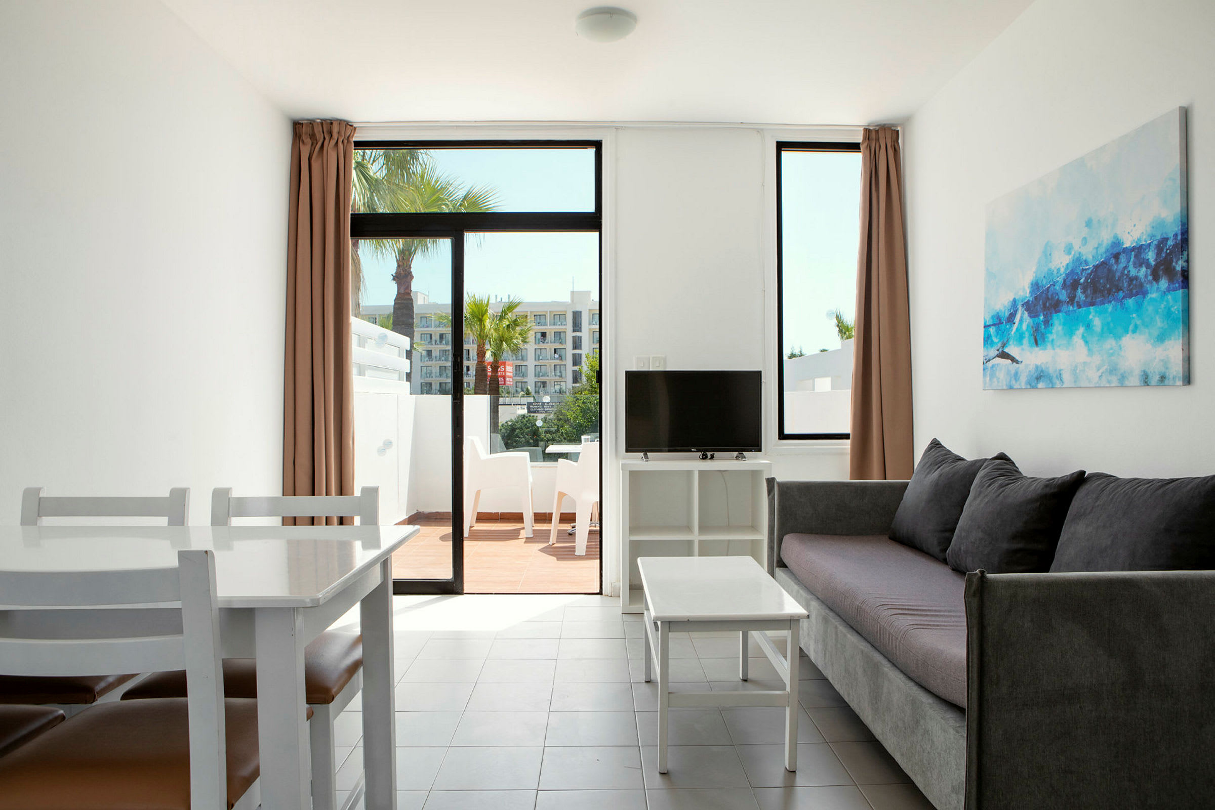 En stue med sofa, salongbord, TV og spisebord. Stor glassdør til en terrasse med utemøbler. (AI-generert tekst)