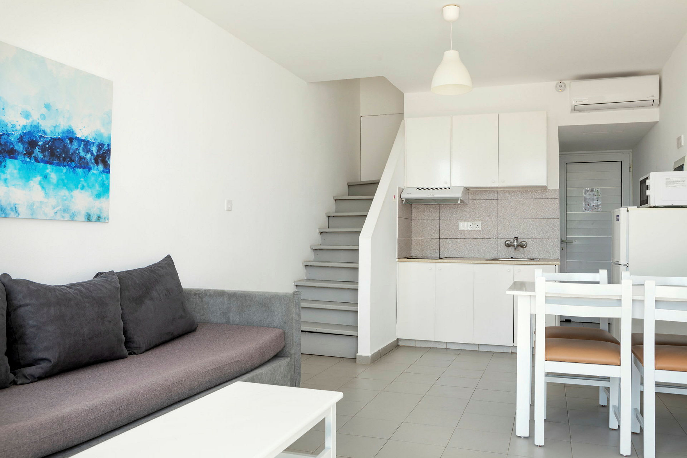 Et moderne møblert rom med grå sofa, kjøkken og spiseområde. (AI-generert tekst)