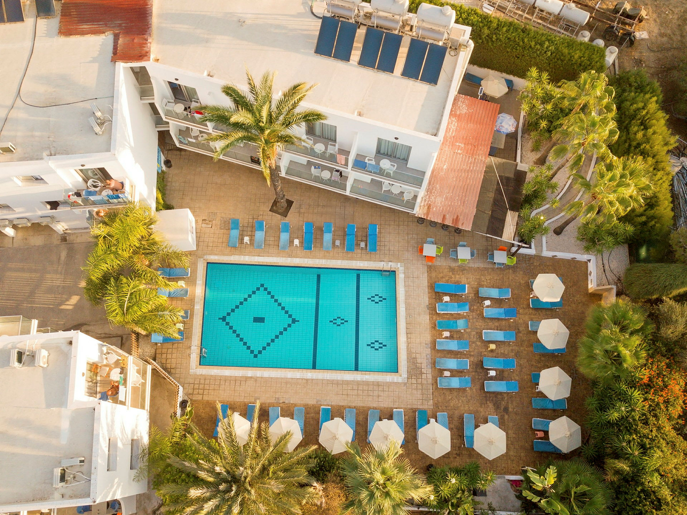 Flyfoto av hotellbasseng med solsenger og parasoller rundt. (AI-generert tekst)