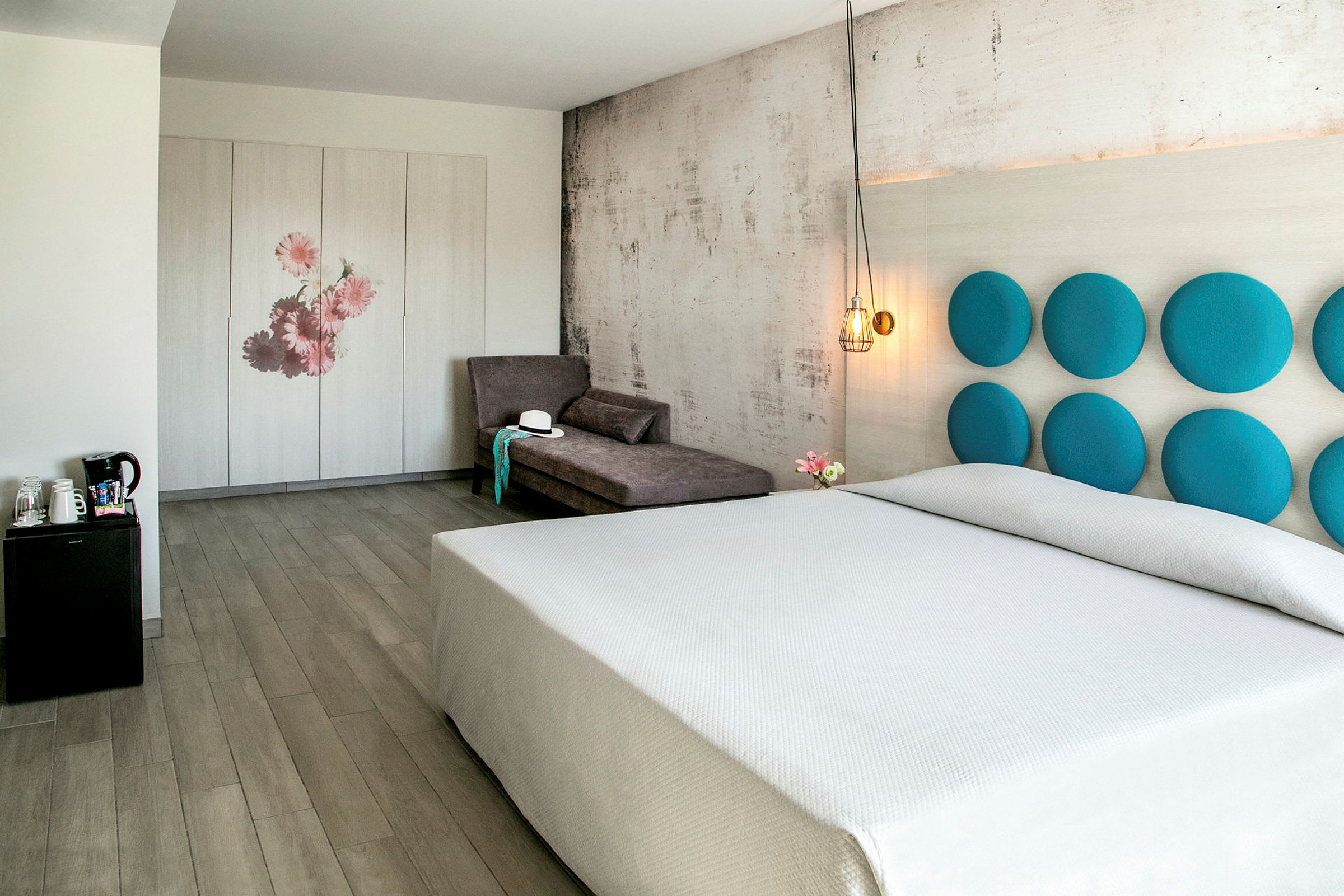 Et lyst hotellrom med en stor seng, en sofa og et skap dekorert med blomster. (AI-generert tekst)