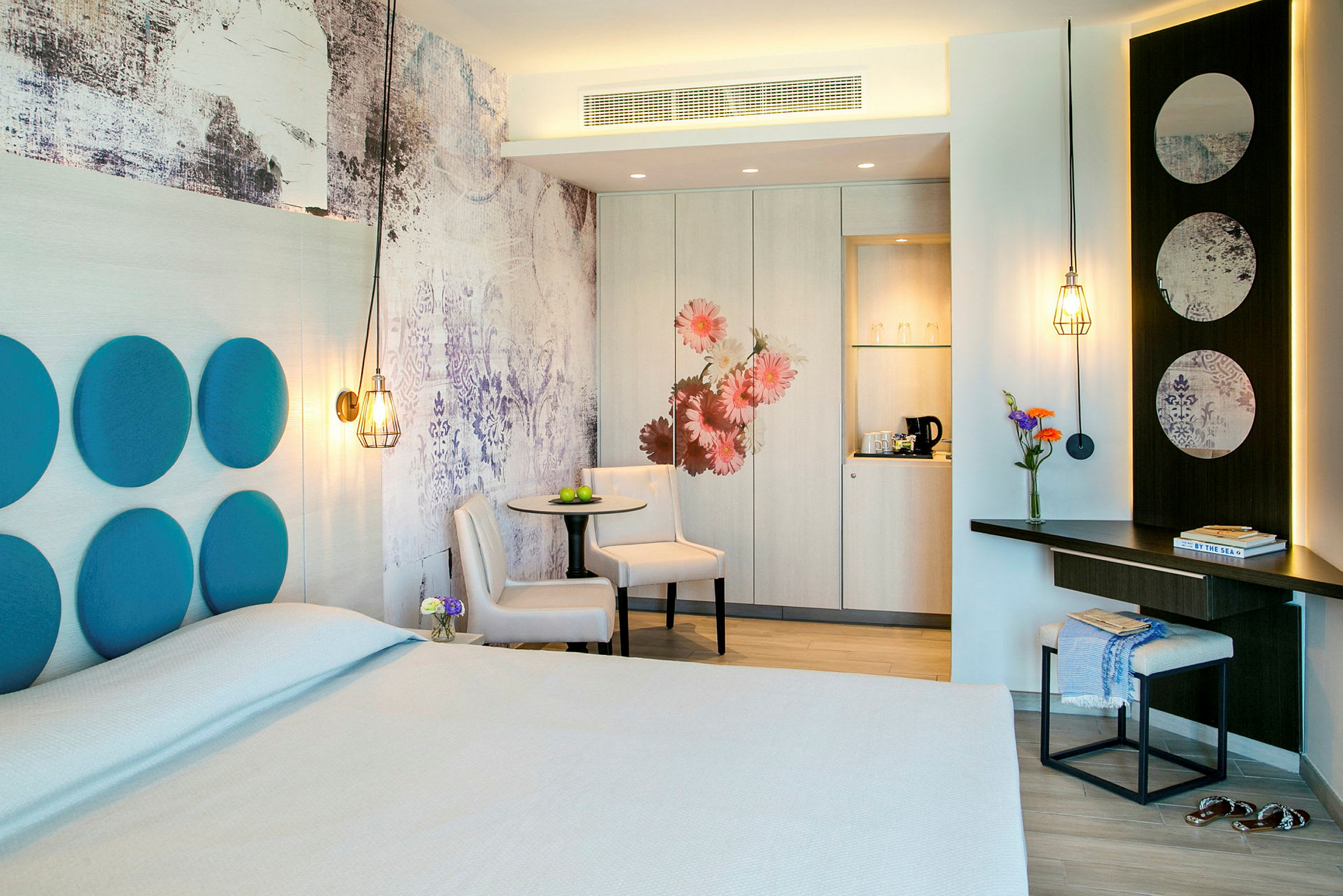 Et hotellrom med moderne design, inkludert en dobbeltseng, bord med stoler, og individuelle designdetaljer som dekorative paneler og belysning. (AI-generert tekst)