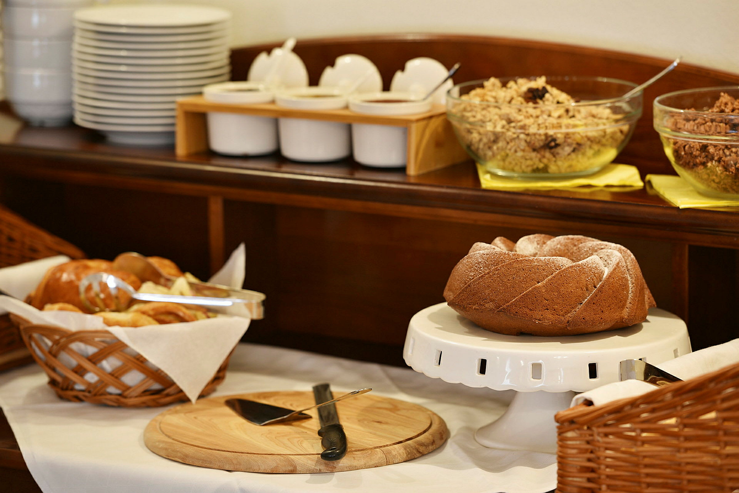 Et frokostbord med brød, en bakst, og boller med müsli og tilbehør. (AI-generert tekst)