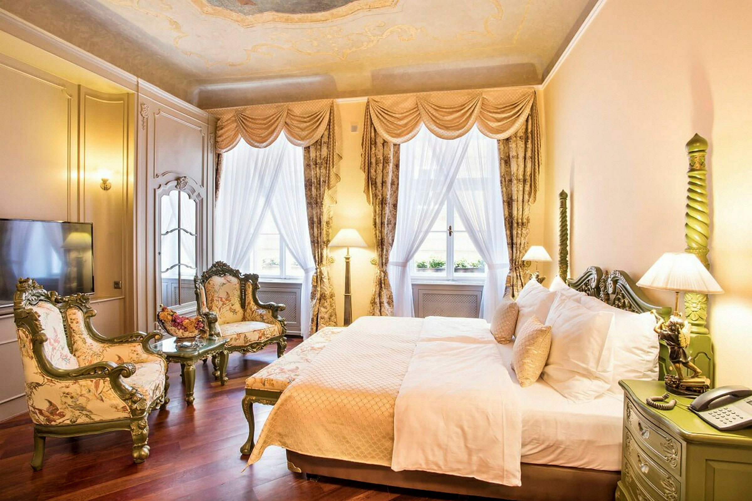 Et elegant hotellrom med seng, to lenestoler og et sofabord. Vinduer med gardiner og myk belysning pryder rommet. (AI-generert tekst)