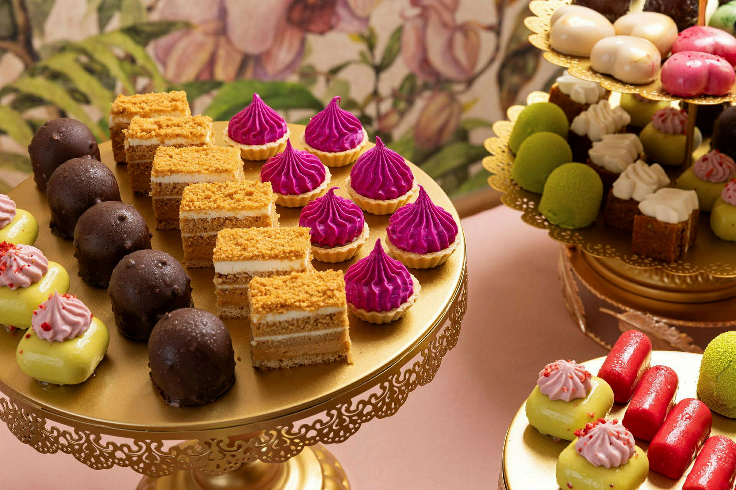 En elegant dessertoppsett på gullfarget serveringsbrett med ulike småkaker, bakverk og konfekt i forskjellige farger. (AI-generert tekst)