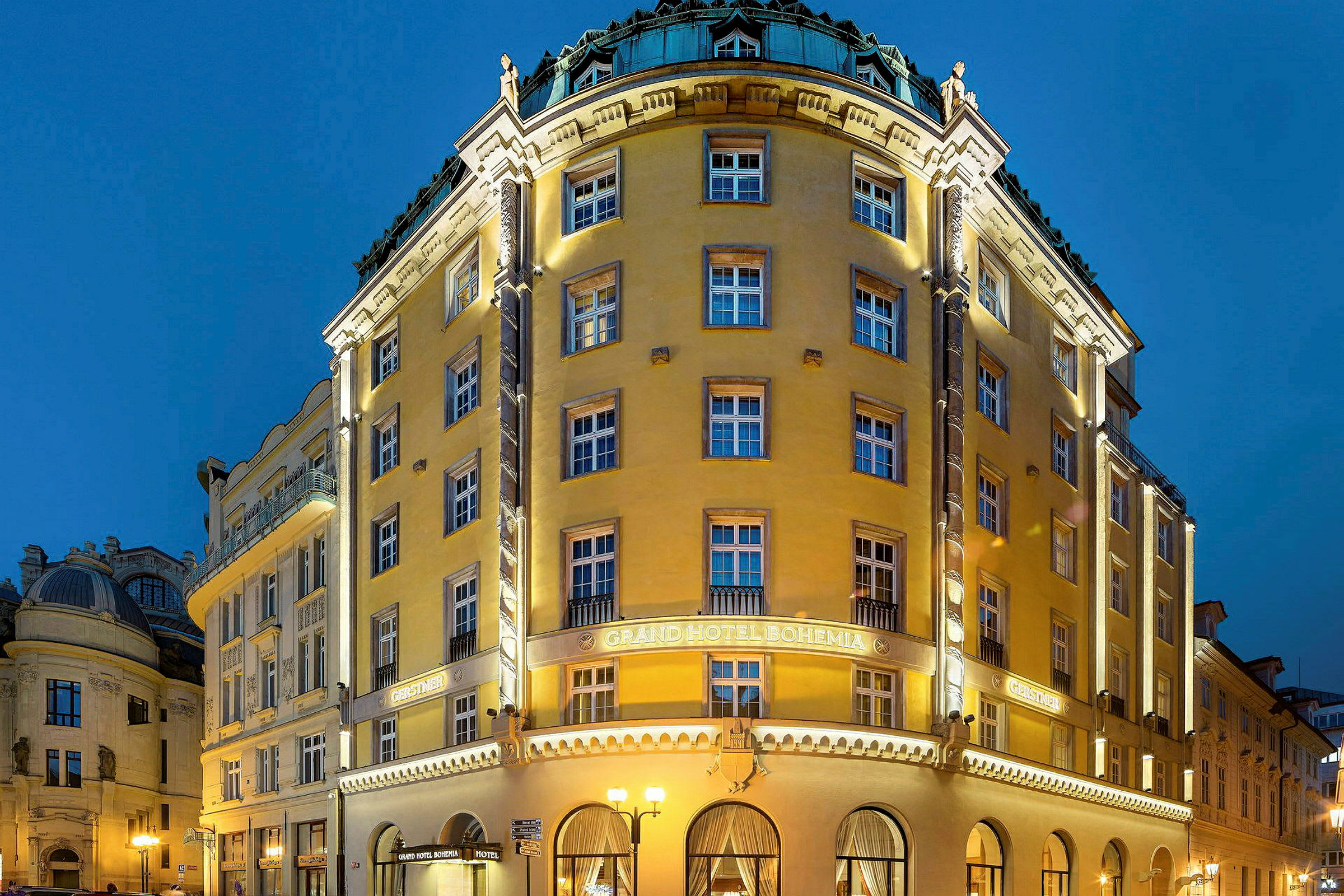 Bilde av en opplyst hotellbygning med buede vinduer og en fasade i gul nyanse. Kveldsbelysning med blå himmel i bakgrunnen. (AI-generert tekst)