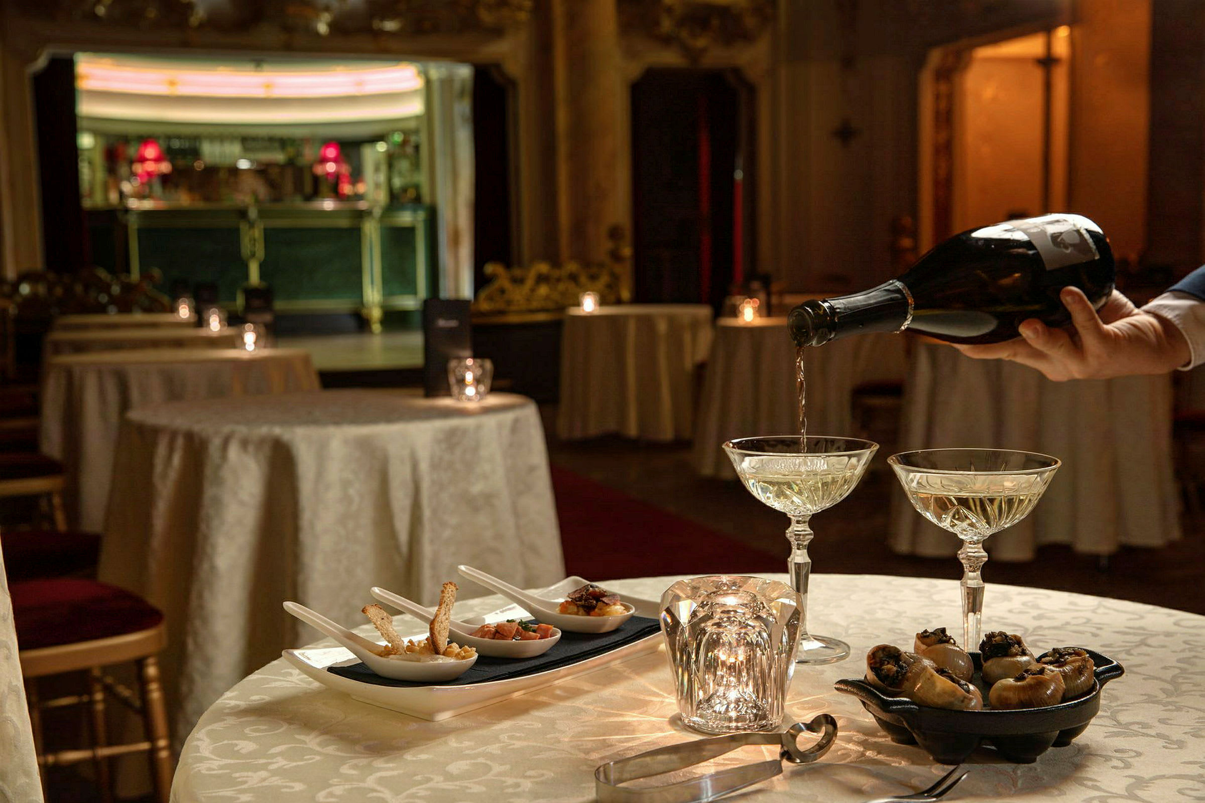 Et bord med glass fylt med champagne, småretter og en lyslykt. Bakgrunnen er en elegant innredet restaurant. (AI-generert tekst)
