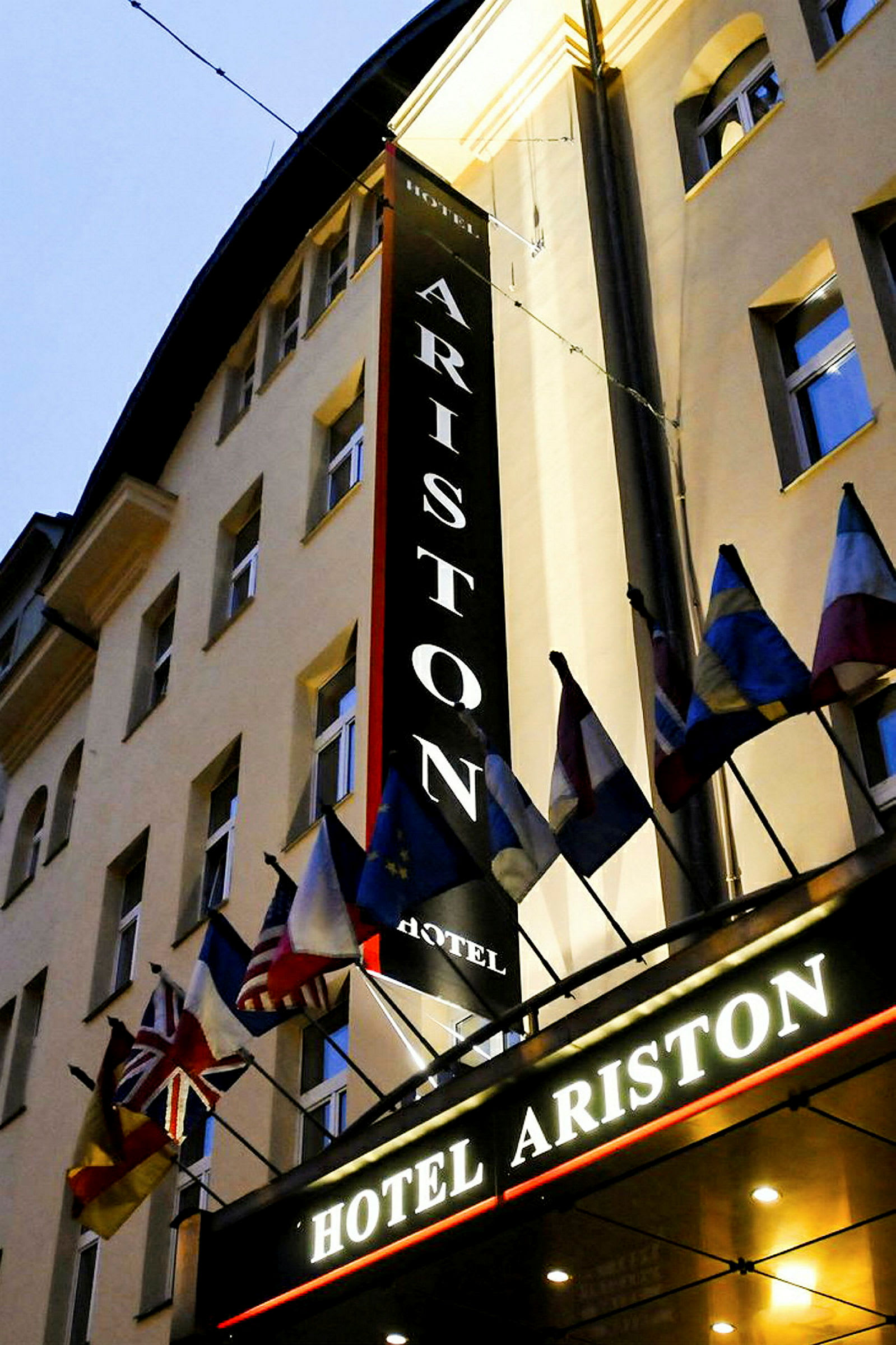 En hotellbygning med skilt som sier 'Hotel Ariston' og flere nasjonalflagg over inngangen. (AI-generert tekst)