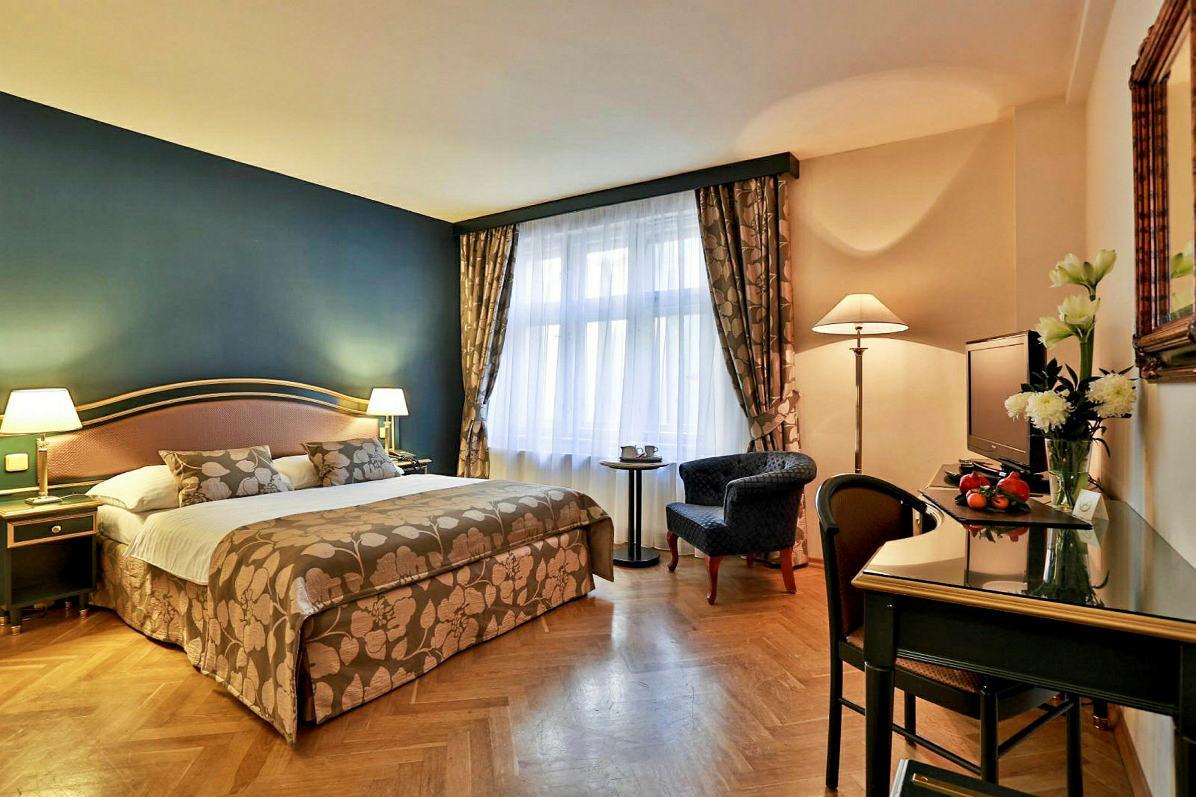 Et hotellrom med en stor seng, skrivebord og stol, lenestol, speil og veranda i bakgrunnen. (AI-generert tekst)