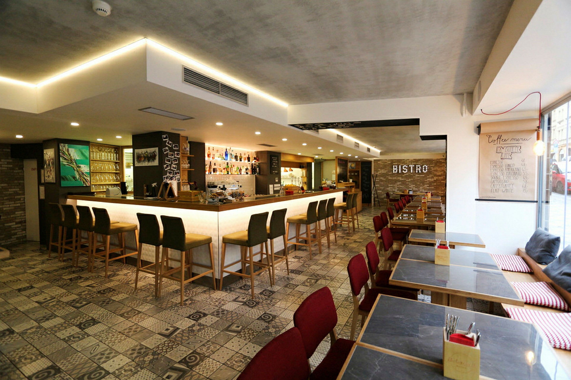 Interiør av en moderne bistro med barkrakker foran en opplyst bardisk og spisebord med røde stoler. (AI-generert tekst)