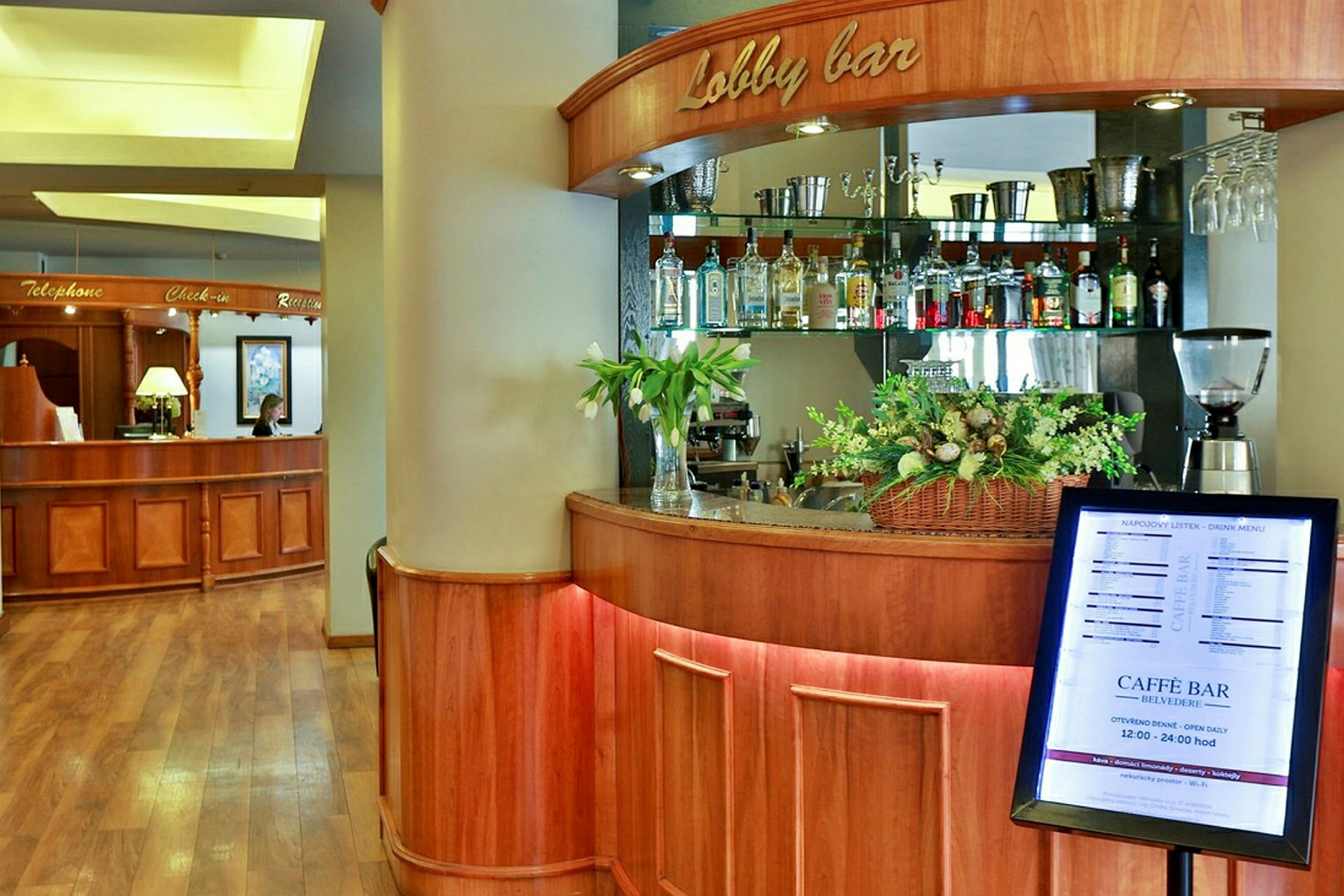 Et hotellobbyområde med en resepsjonsdisk i tre på venstre side og en lobbybar med drikkeflasker og blomsterdekorasjoner på høyre side. (AI-generert tekst)