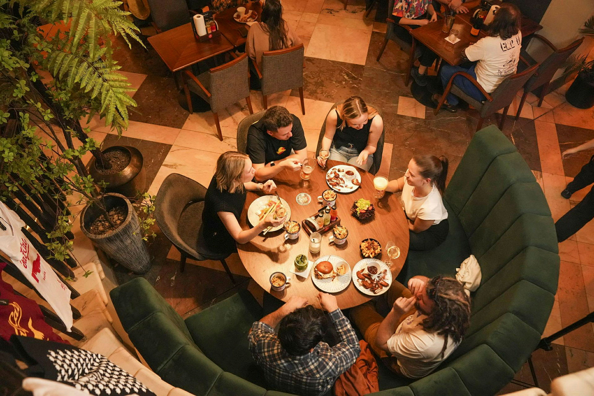 Fem personer sitter rundt et rundt bord på en restaurant og spiser og drikker. (AI-generert tekst)