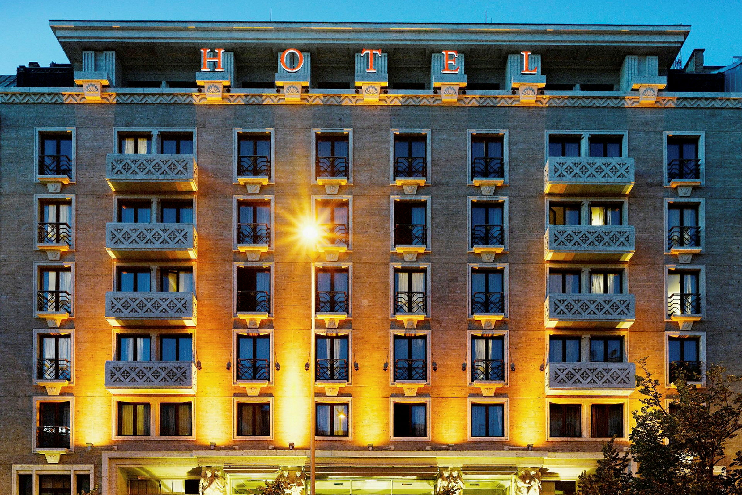 En flerfarget hotellbygning med balkonger og en stor opplyst skiltinskripsjon "HOTEL" på toppen. (AI-generert tekst)