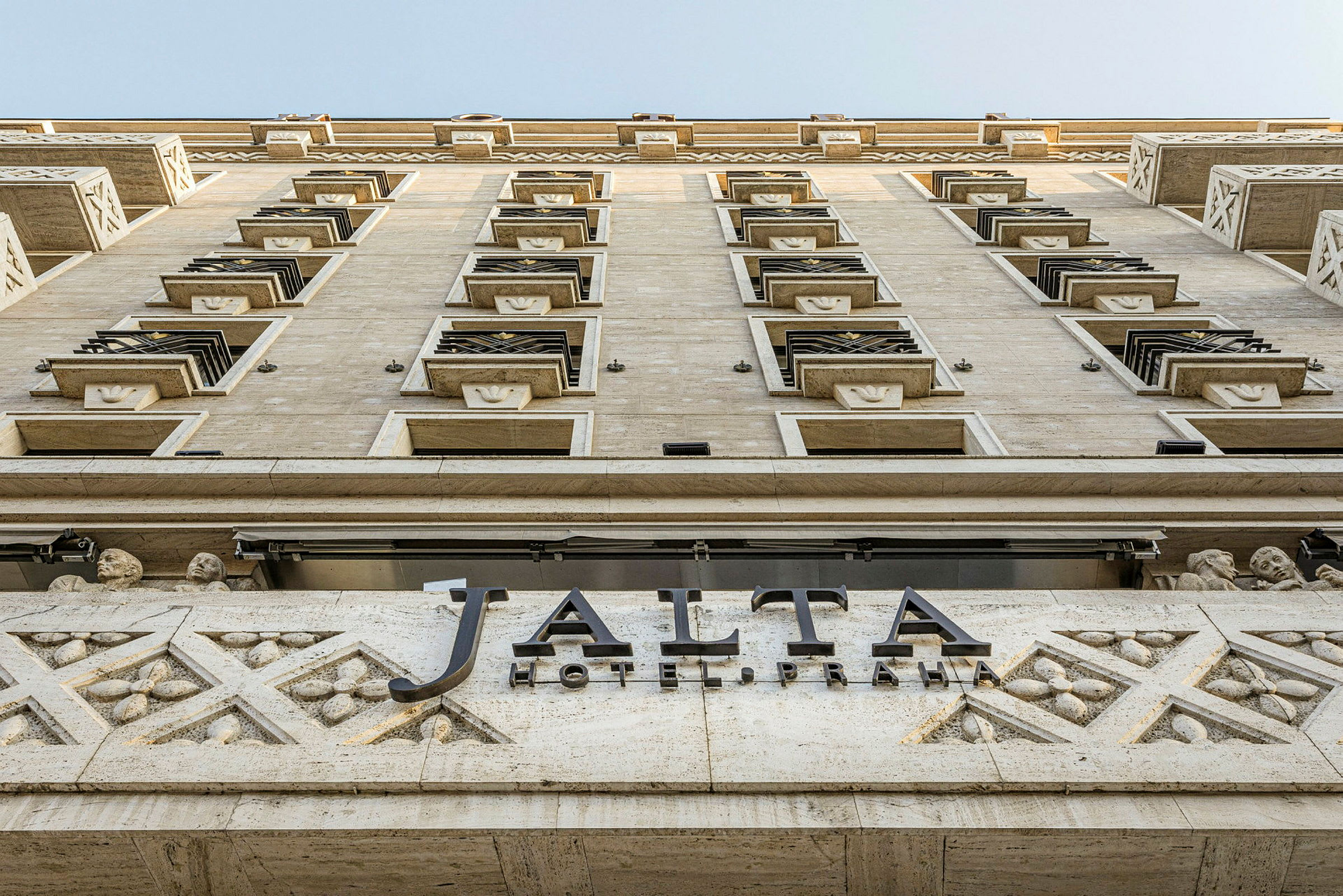 En bygningsfasade fotografert nedenfra og opp, med et skilt som sier "Jalta Hotel Praha". (AI-generert tekst)