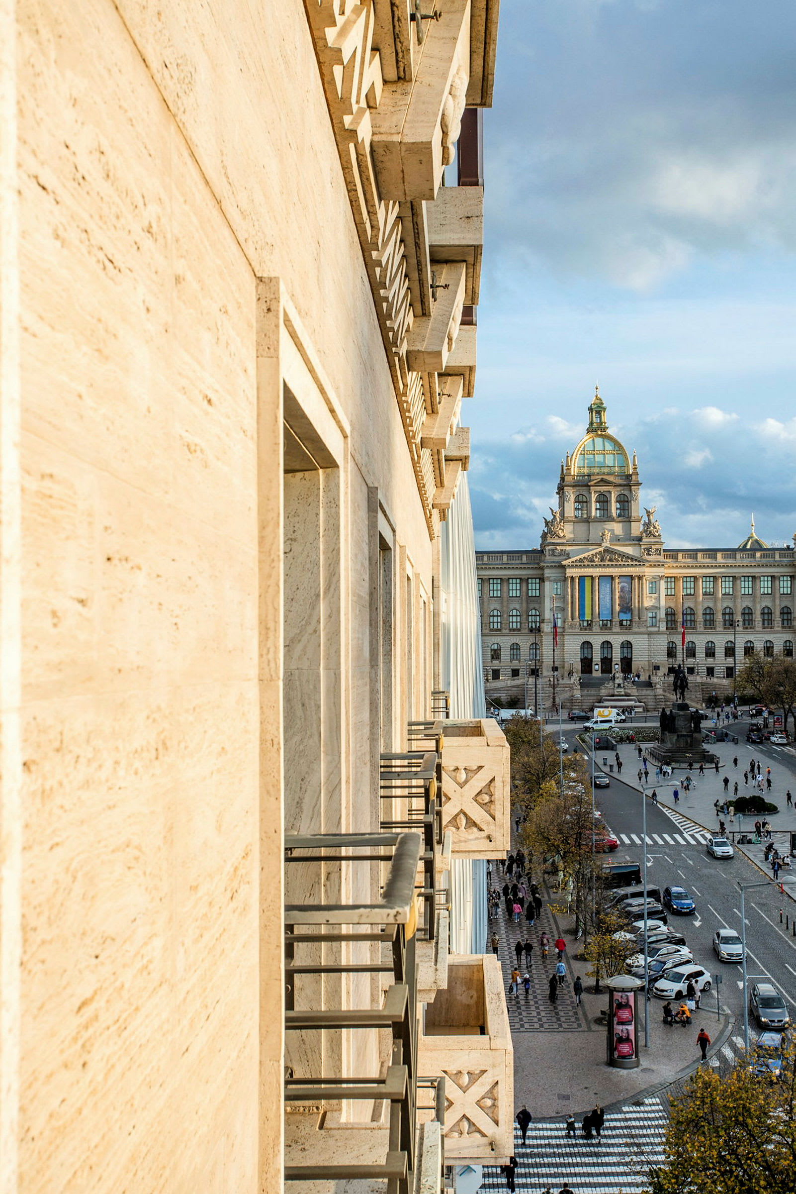 Bilde av en bygningfasade i forgrunnen og en bygning med en kuppel i bakgrunnen, samt en travel gate med mennesker og trafikk i midten. (AI-generert tekst)