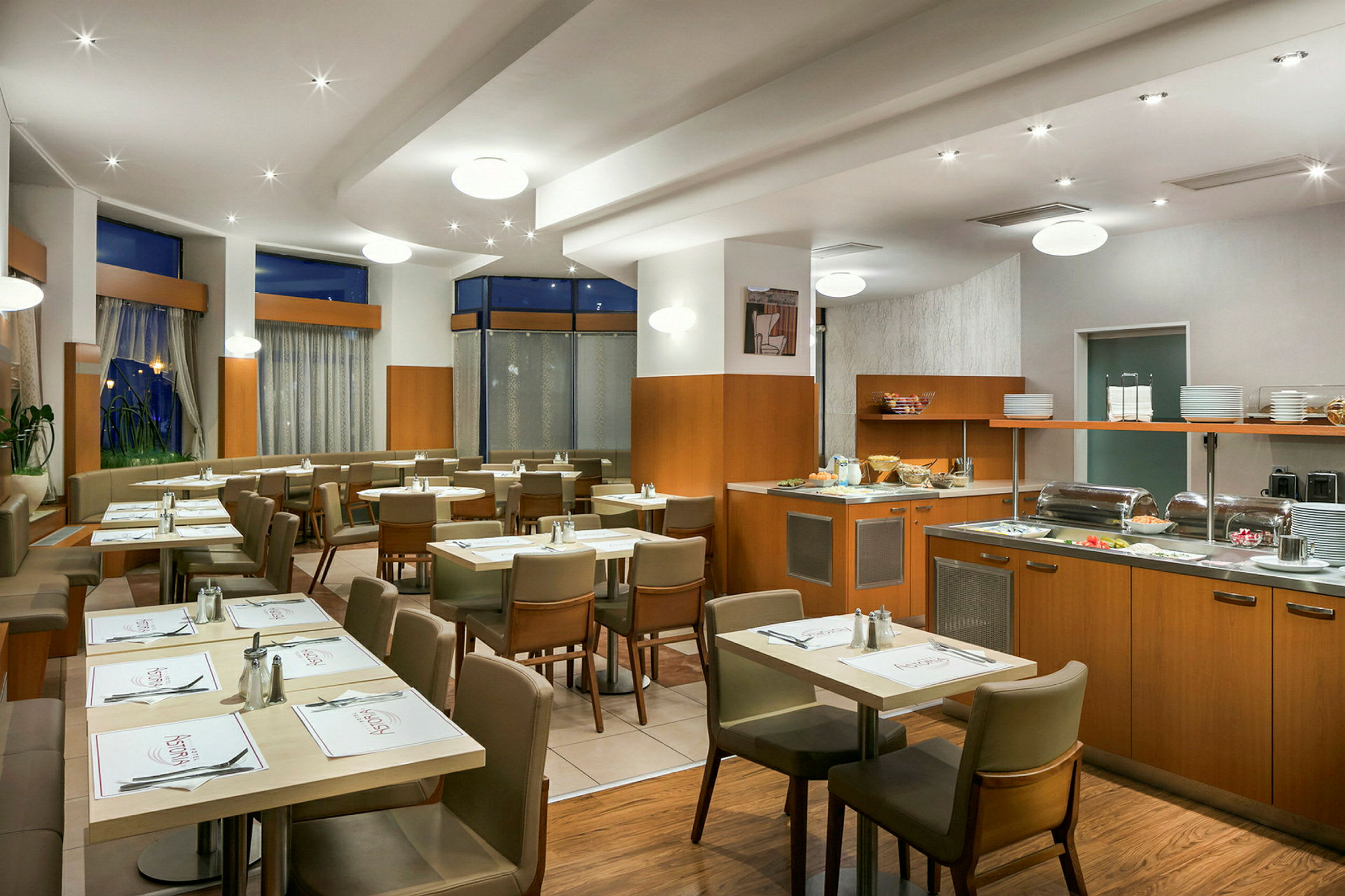 Interiør av en restaurant med bord og stoler samt en bufféservering. (AI-generert tekst)