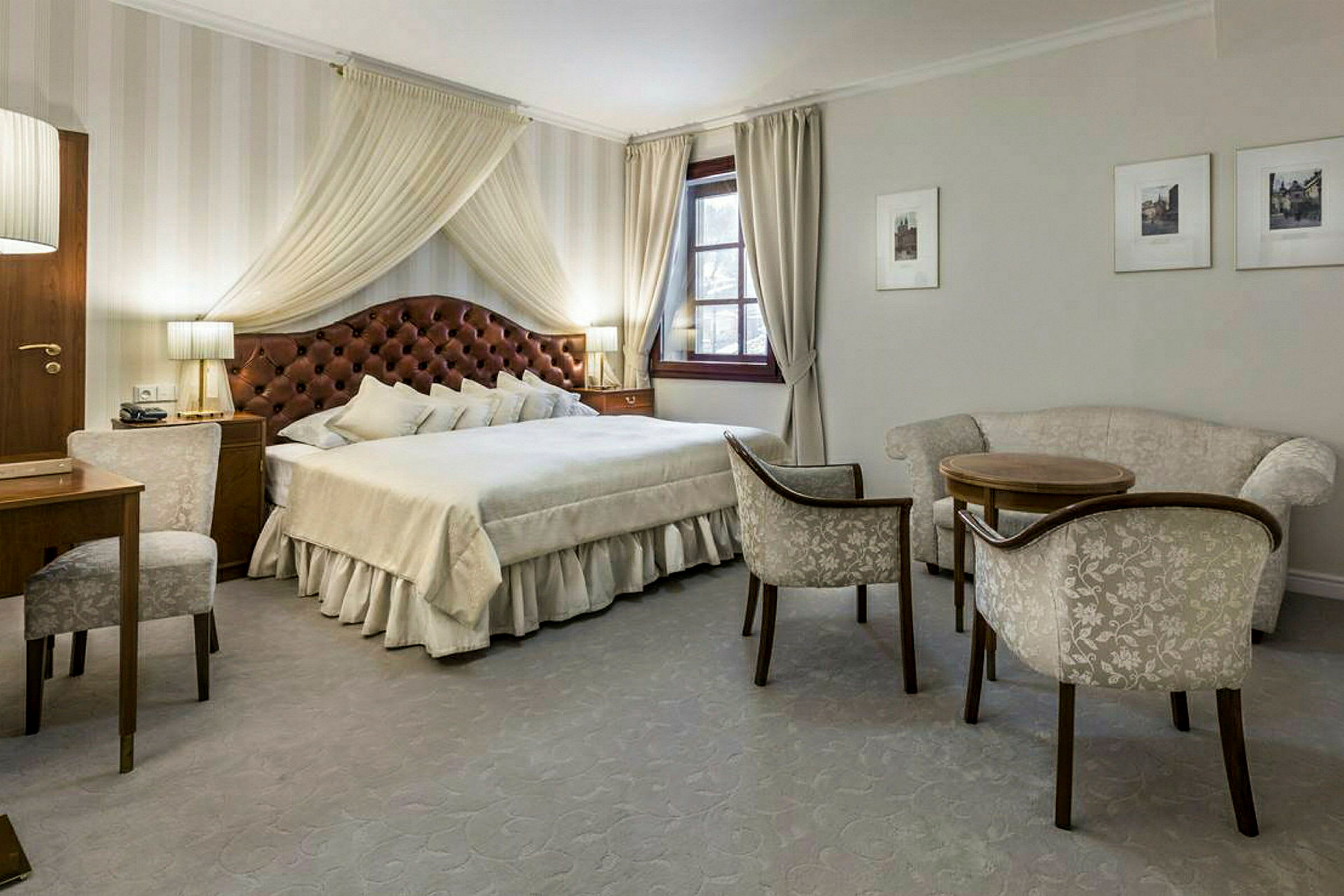 Et elegant innredet soverom med en stor dobbeltseng, komfortable sittemøbler, et skrivebord og vinduer med gardiner. (AI-generert tekst)