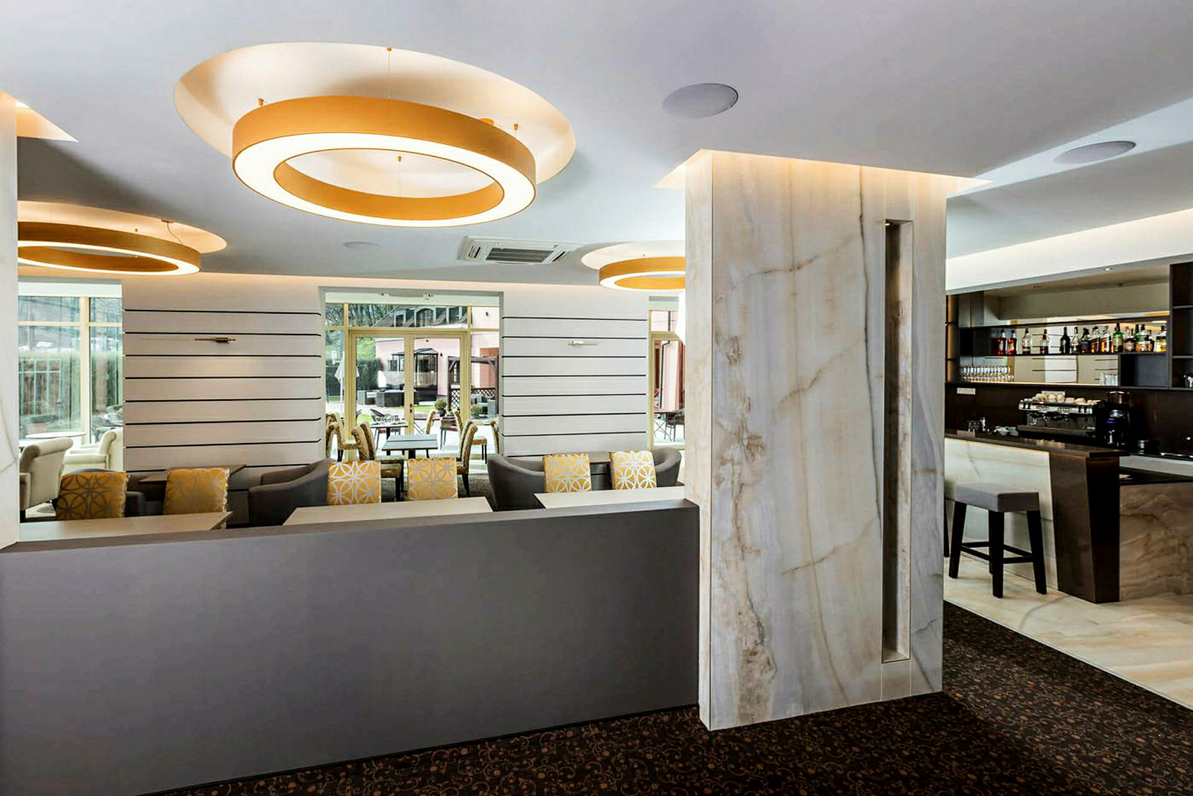 Interiør av en moderne lounge med sofaer, barområde og store dekorative lysringer i taket. (AI-generert tekst)