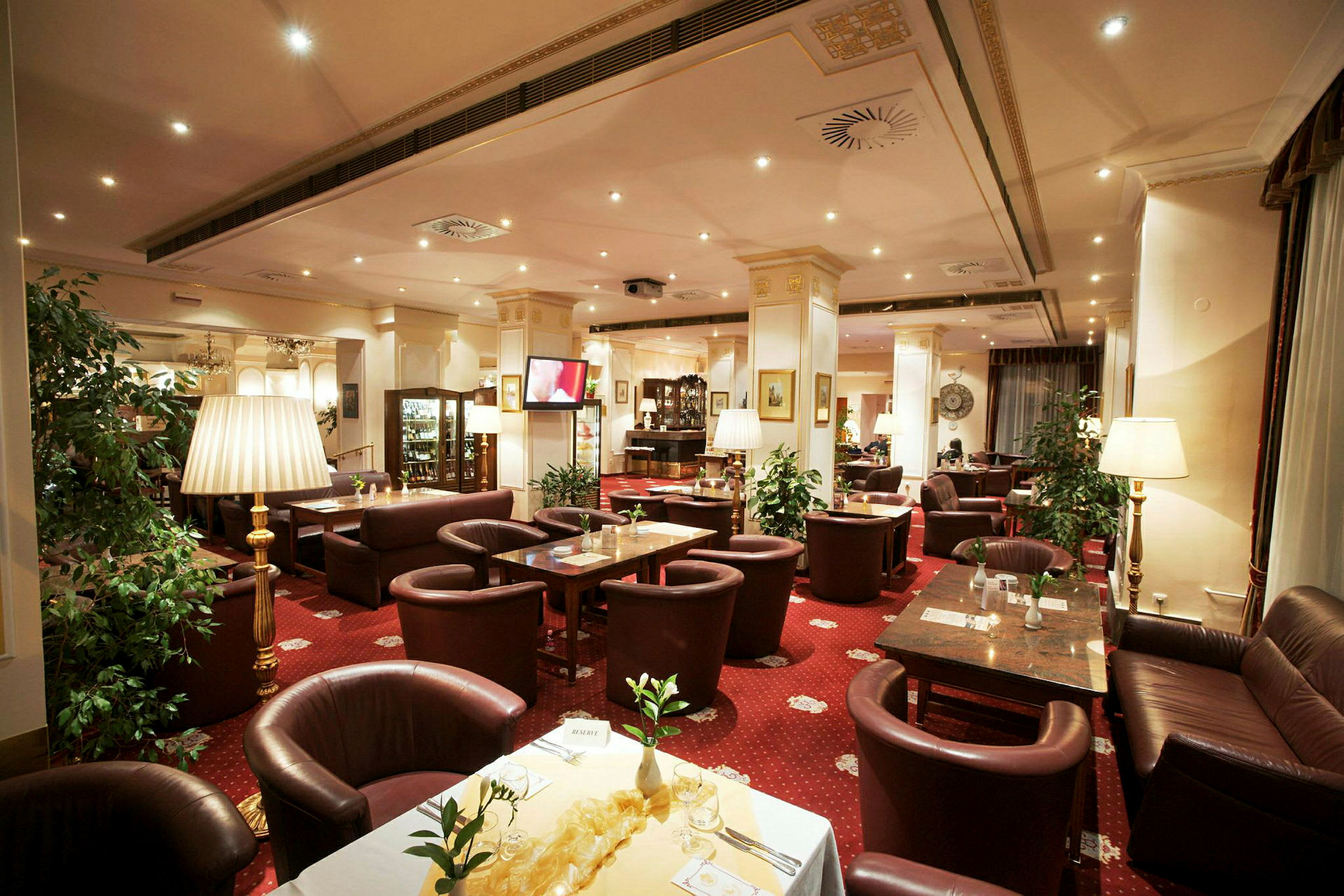 Bilde av en elegant restaurant med røde tepper, brune lærsofaer og stoler samt dekorerte bord. (AI-generert tekst)