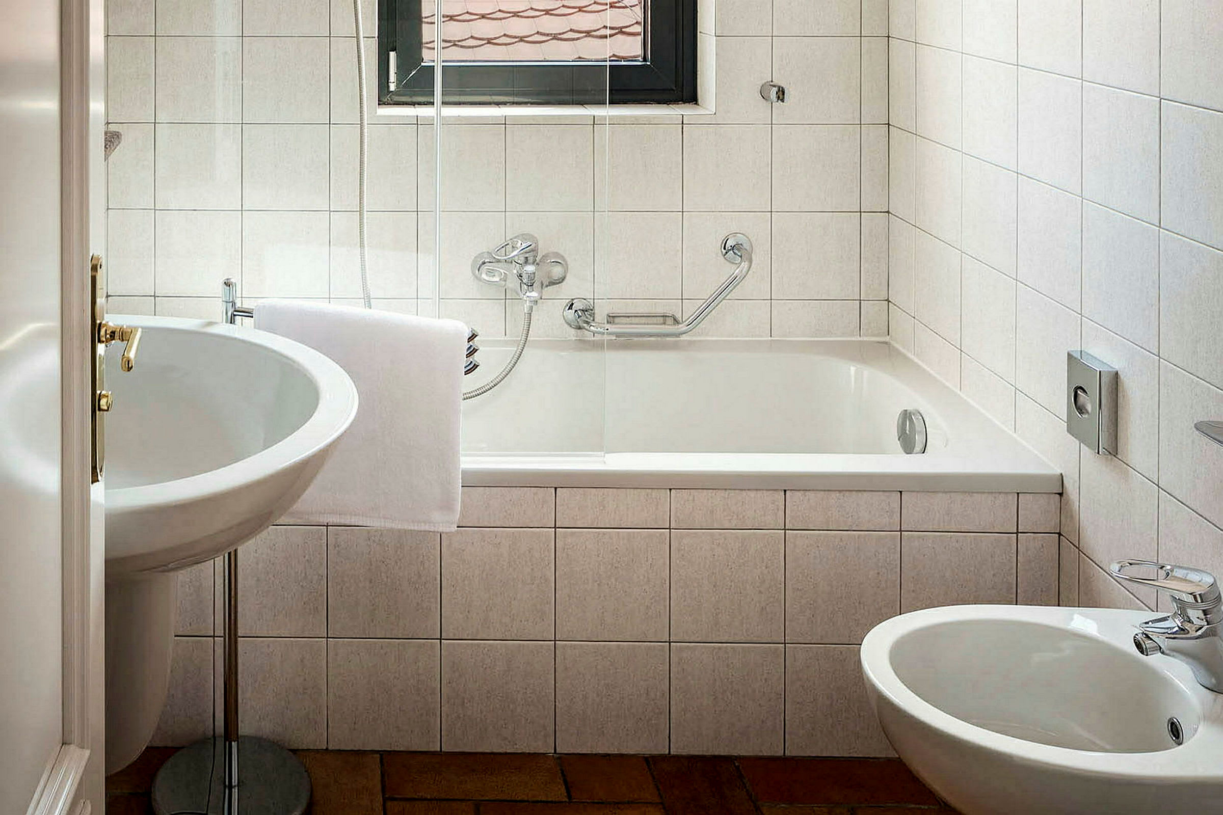 Et bad med badekar, servant og bidet. Hvite fliser på veggene. (AI-generert tekst)