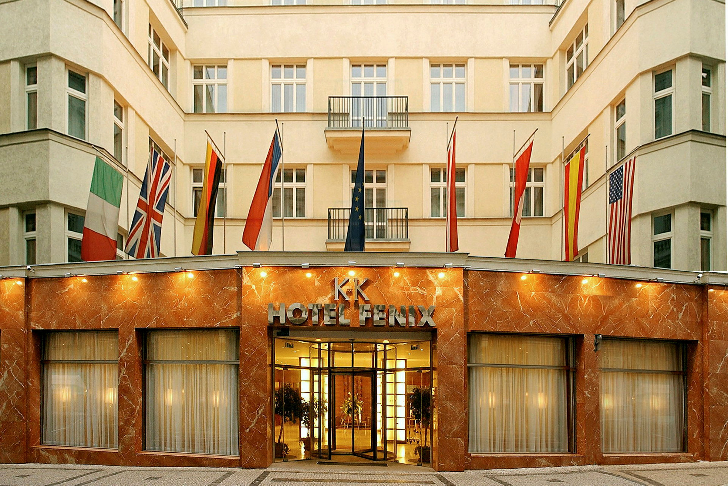 Bygningen er et hotell med fasade av marmor og glass samt flere flagg ved inngangen. (AI-generert tekst)