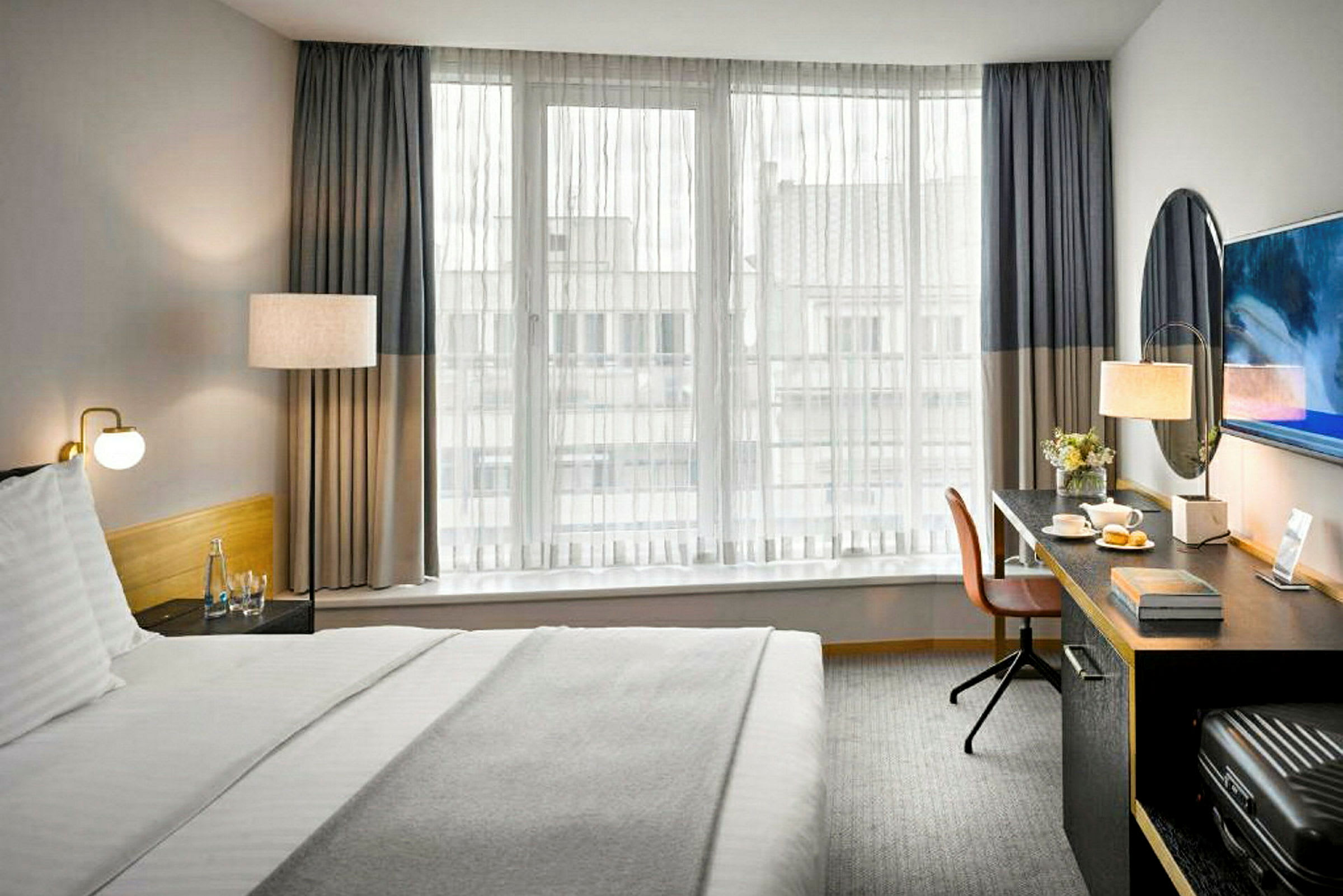 Et hotellrom med en seng, et skrivebord og et vindu med tynne gardiner. (AI-generert tekst)