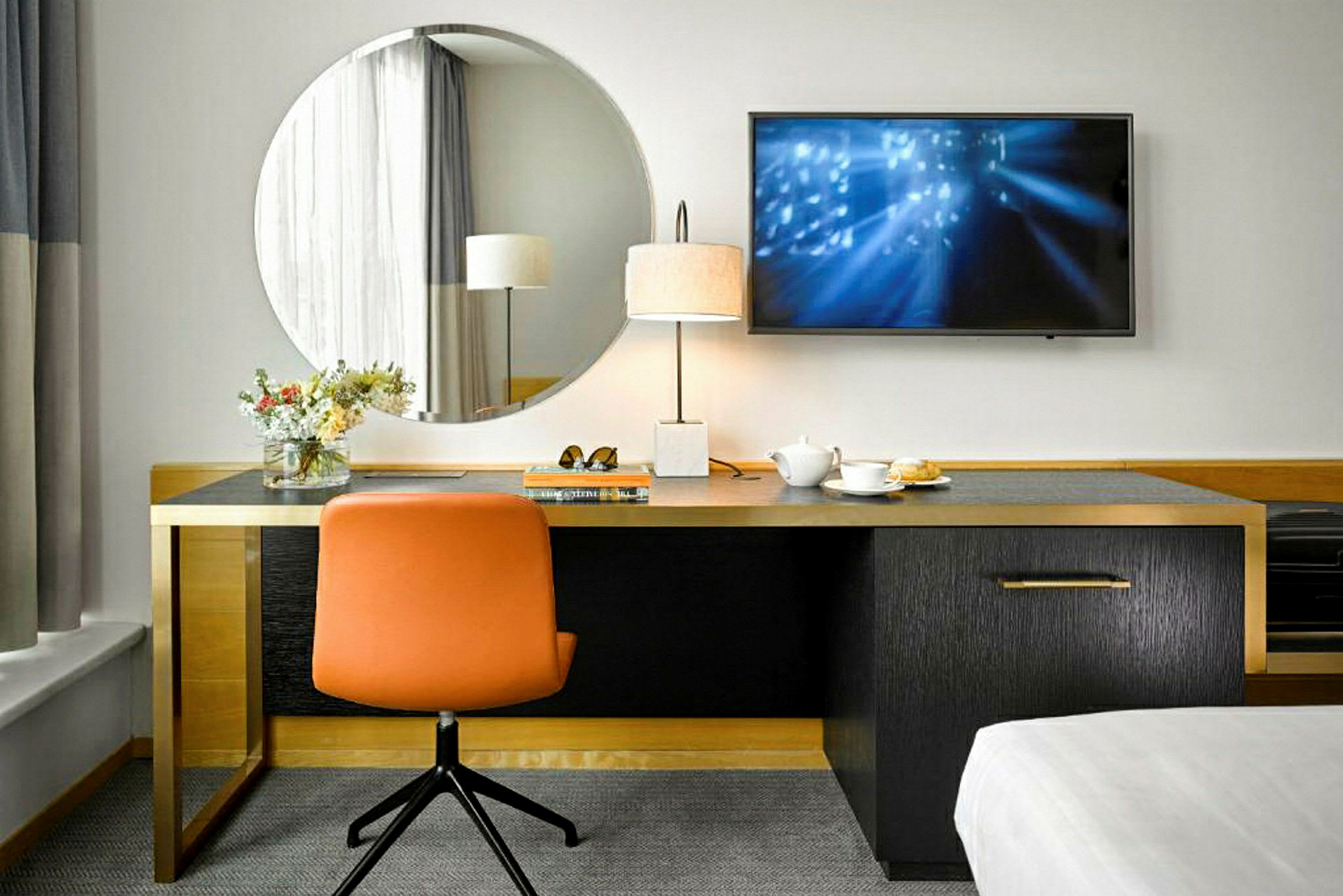 Et skrivebord med et rundt speil over, en oransje stol og en bordlampe ved siden av. En kopp te og noen gjenstander ligger på skrivebordet. (AI-generert tekst)