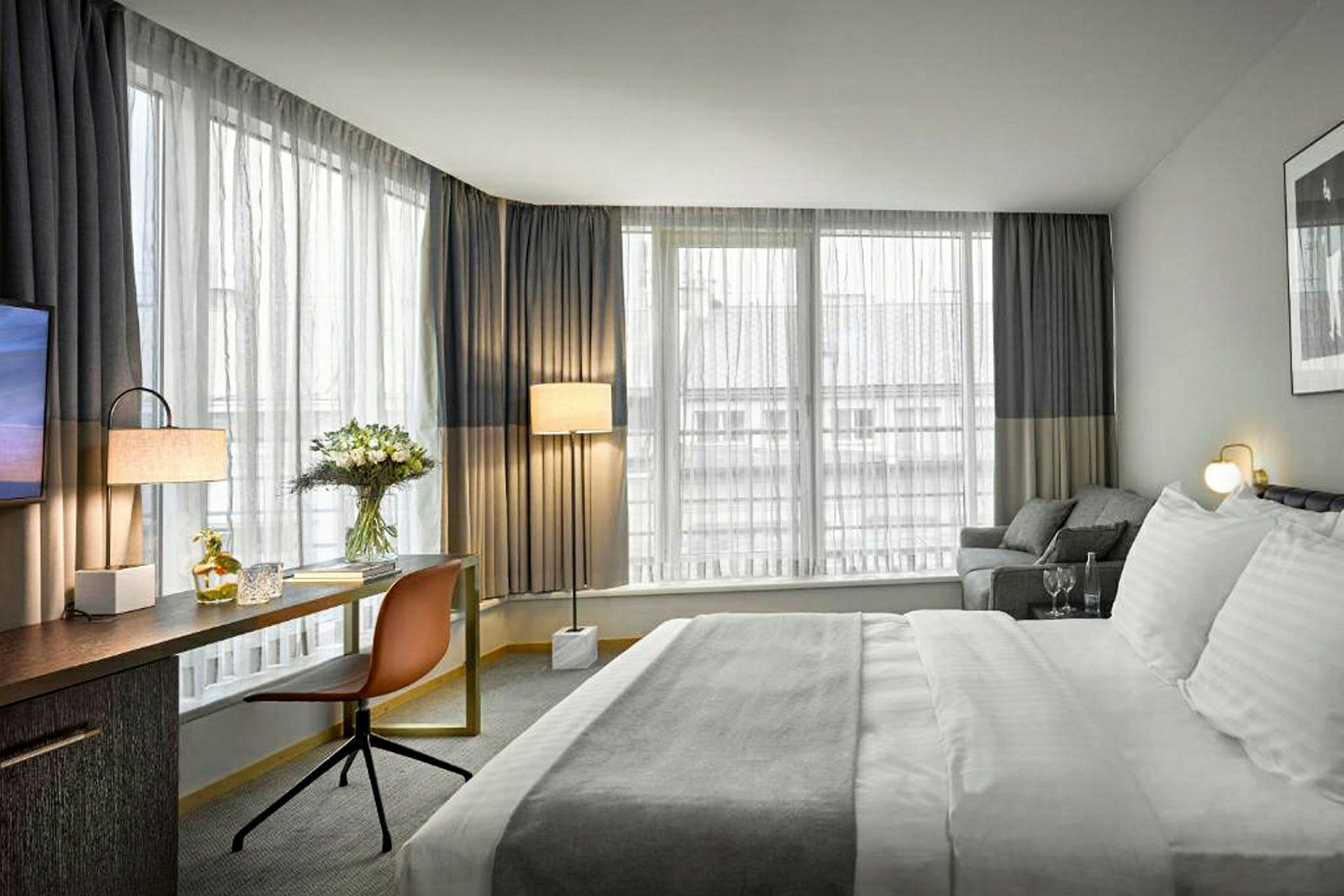 Et hotellrom med stor seng, skrivebord, stol og vinduer med gardiner. (AI-generert tekst)
