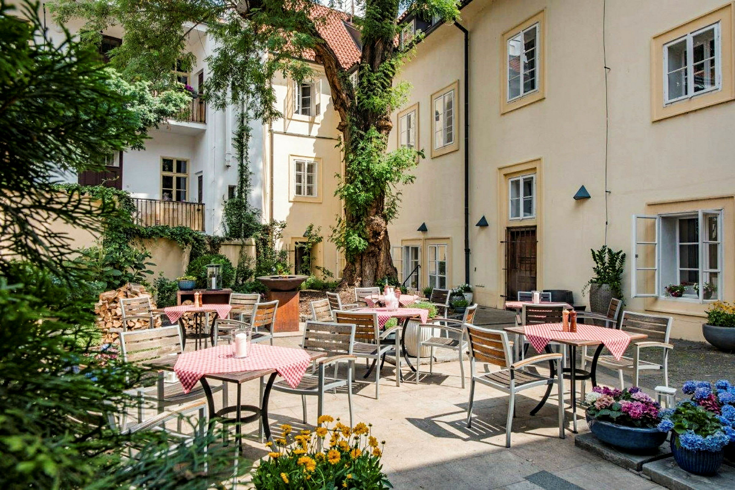 En bakgård med uteservering. Bord med rødrutete duker, stoler og planter er synlige. (AI-generert tekst)