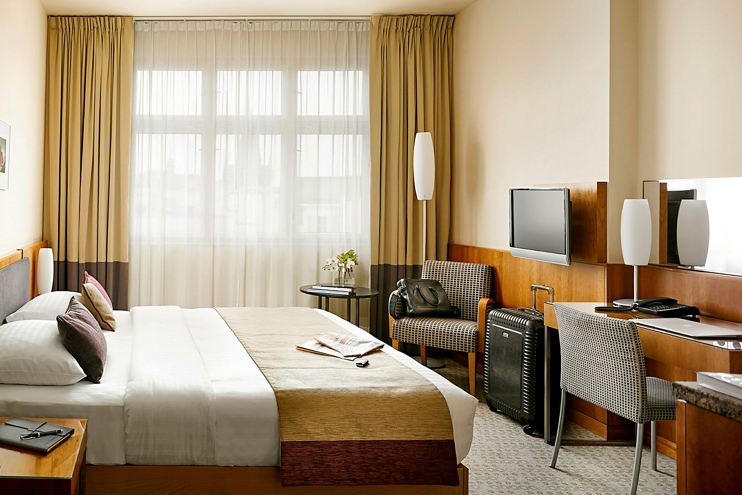 Et hotellrom med en stor seng, skrivebord og stol, samt en lenestol og en koffert. (AI-generert tekst)