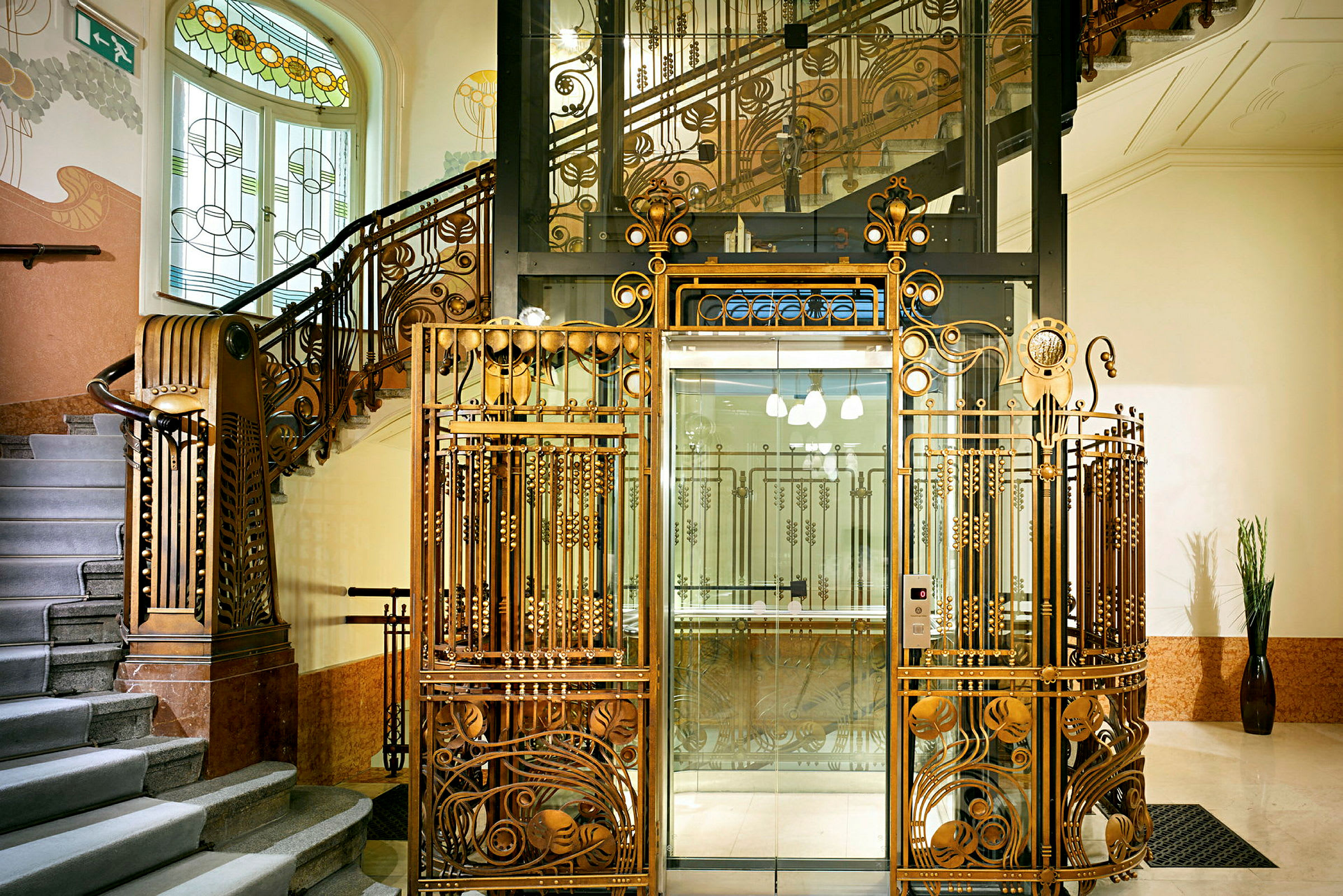 En vakker Art Nouveau-trapp med dekorerte jernrekkverk og en glassheis omgitt av et dekorert metallstakitt. (AI-generert tekst)