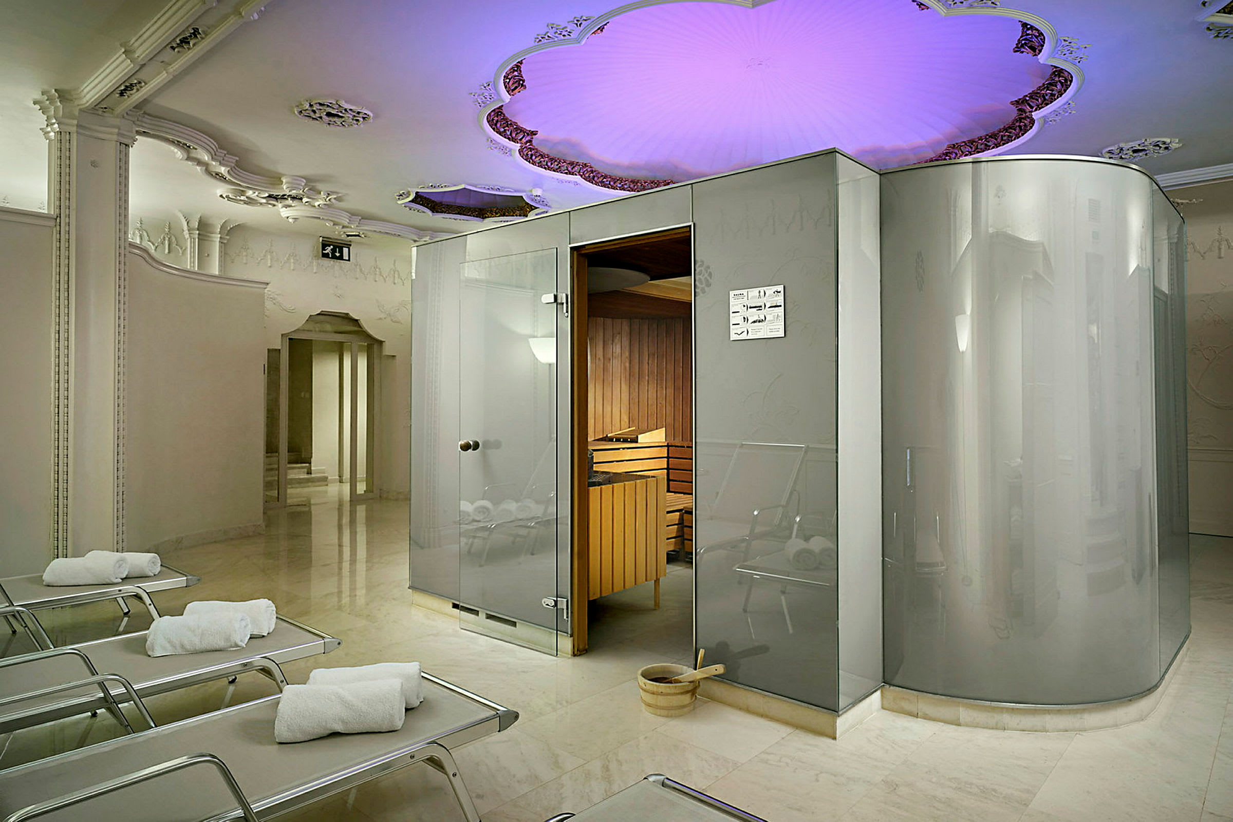 Bildet viser et moderne spa med en badstue og loungemøbler. Taket er dekorert med farget belysning. (AI-generert tekst)