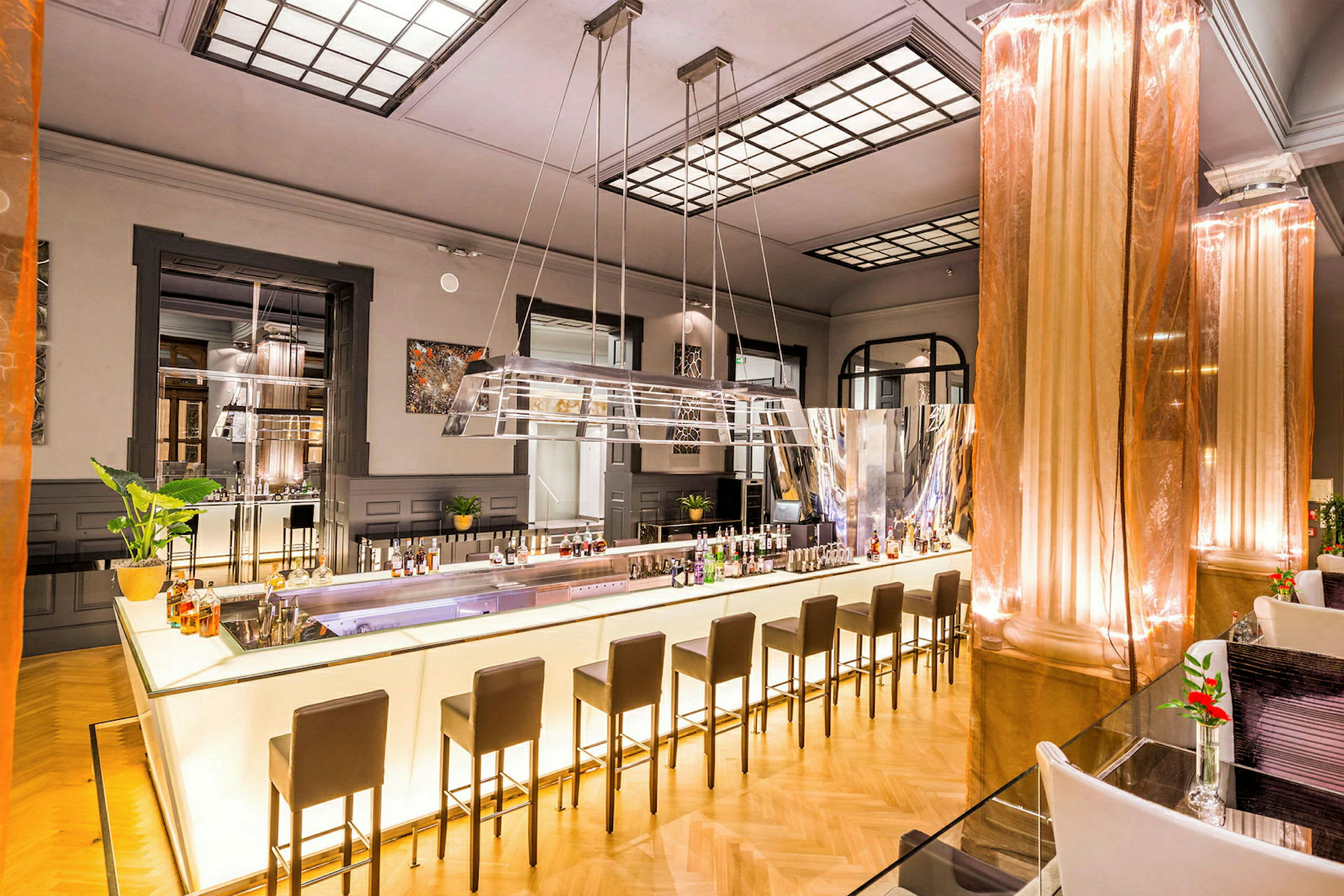 Bilde av en moderne bar med lys belysning. Baren har høye stoler og er dekorert med flasker og planter. (AI-generert tekst)