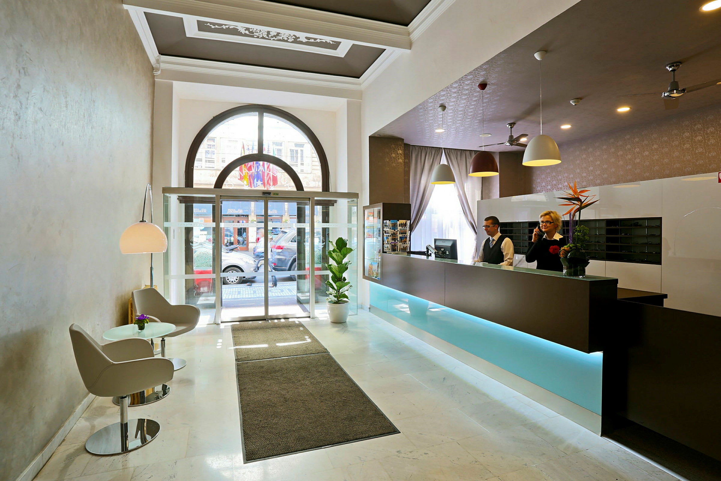 Hotellobby med resepsjon, sittegruppe og glassdører mot utsiden. (AI-generert tekst)