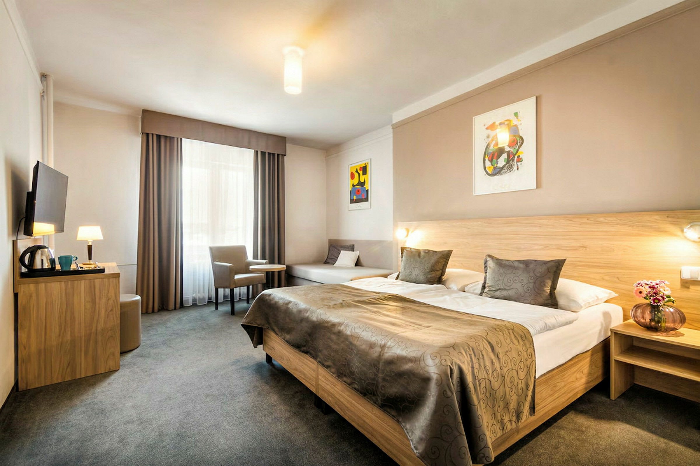 Et hotellrom med en stor dobbeltseng, et bord med to stoler og en veggmontert TV. (AI-generert tekst)