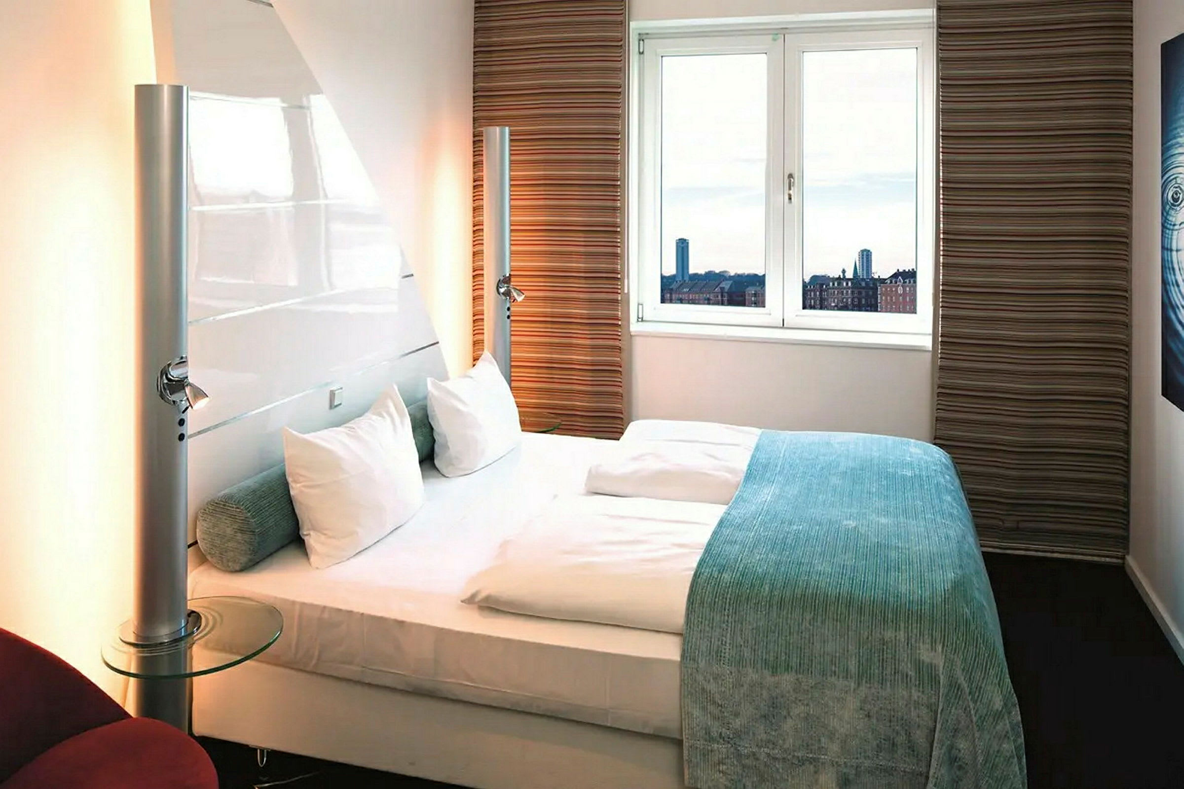 Et hotellrom med en dobbeltseng, to puter og et vindu som viser en byutsikt. (AI-generert tekst)