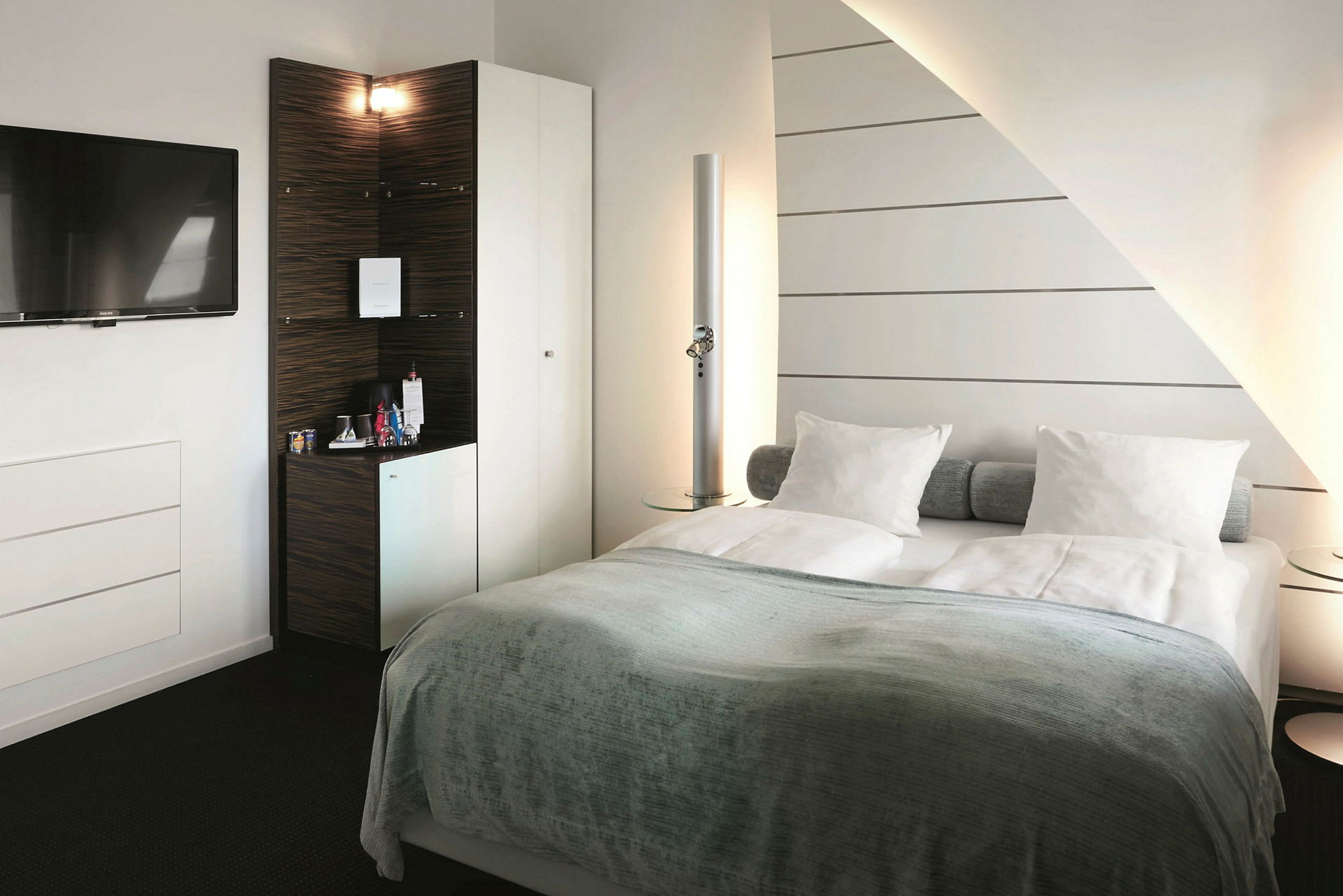 Et hotellrom med en dobbeltseng, veggmontert TV og minibarskap. (AI-generert tekst)