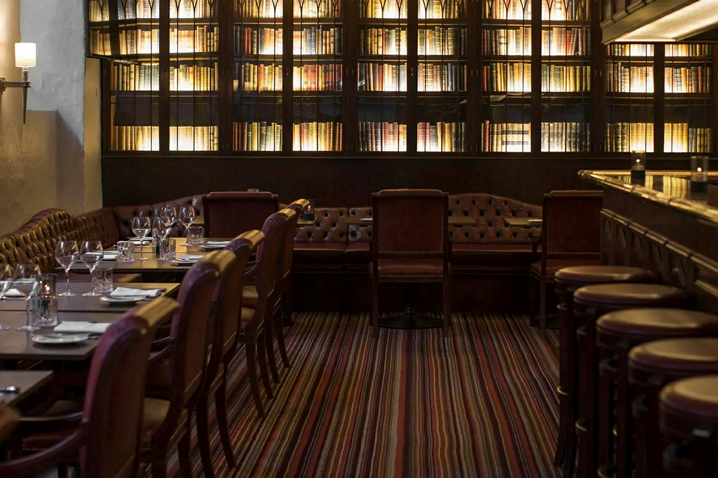 Restaurant med sitteplasser for gjester med brune stoler, en bibliotekinspirert veggseksjon og stemningsfull belysning. (AI-generert tekst)