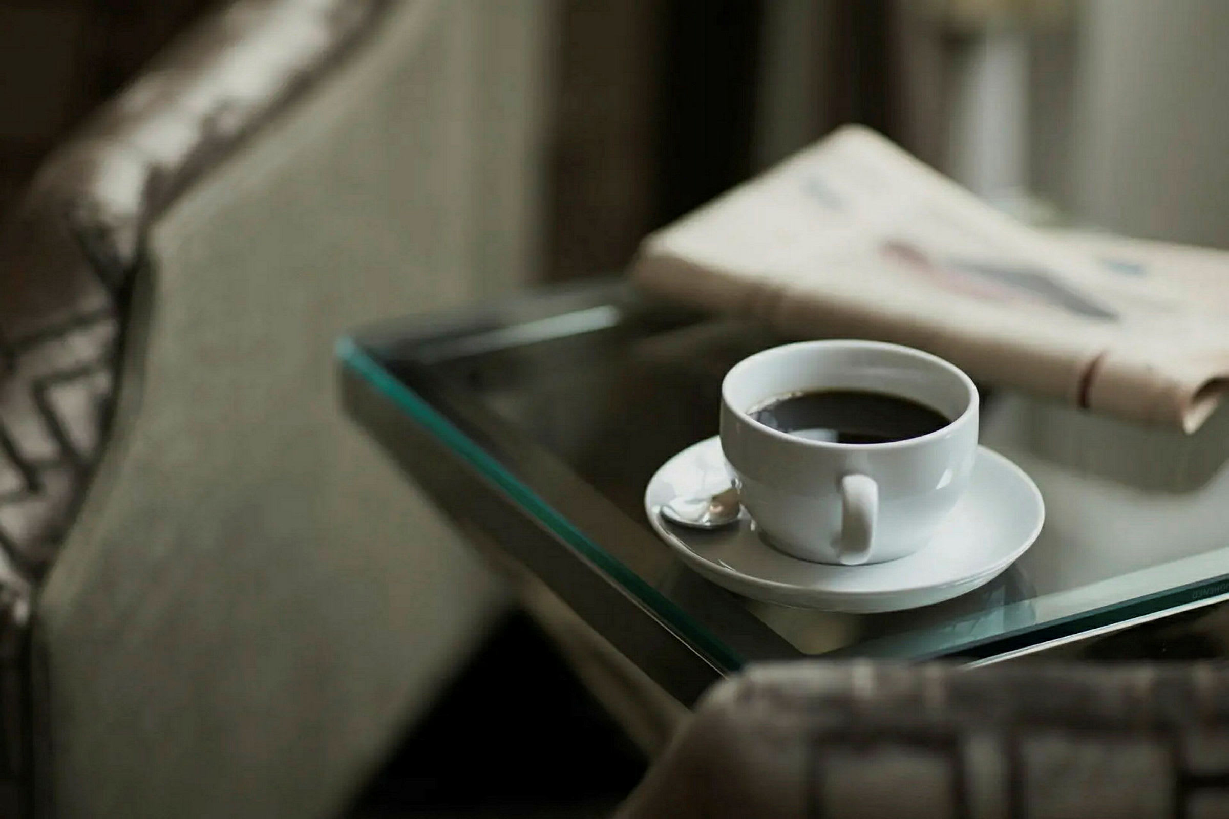En kopp kaffe står på et glassbord ved siden av en sammenbrettet avis. (AI-generert tekst)