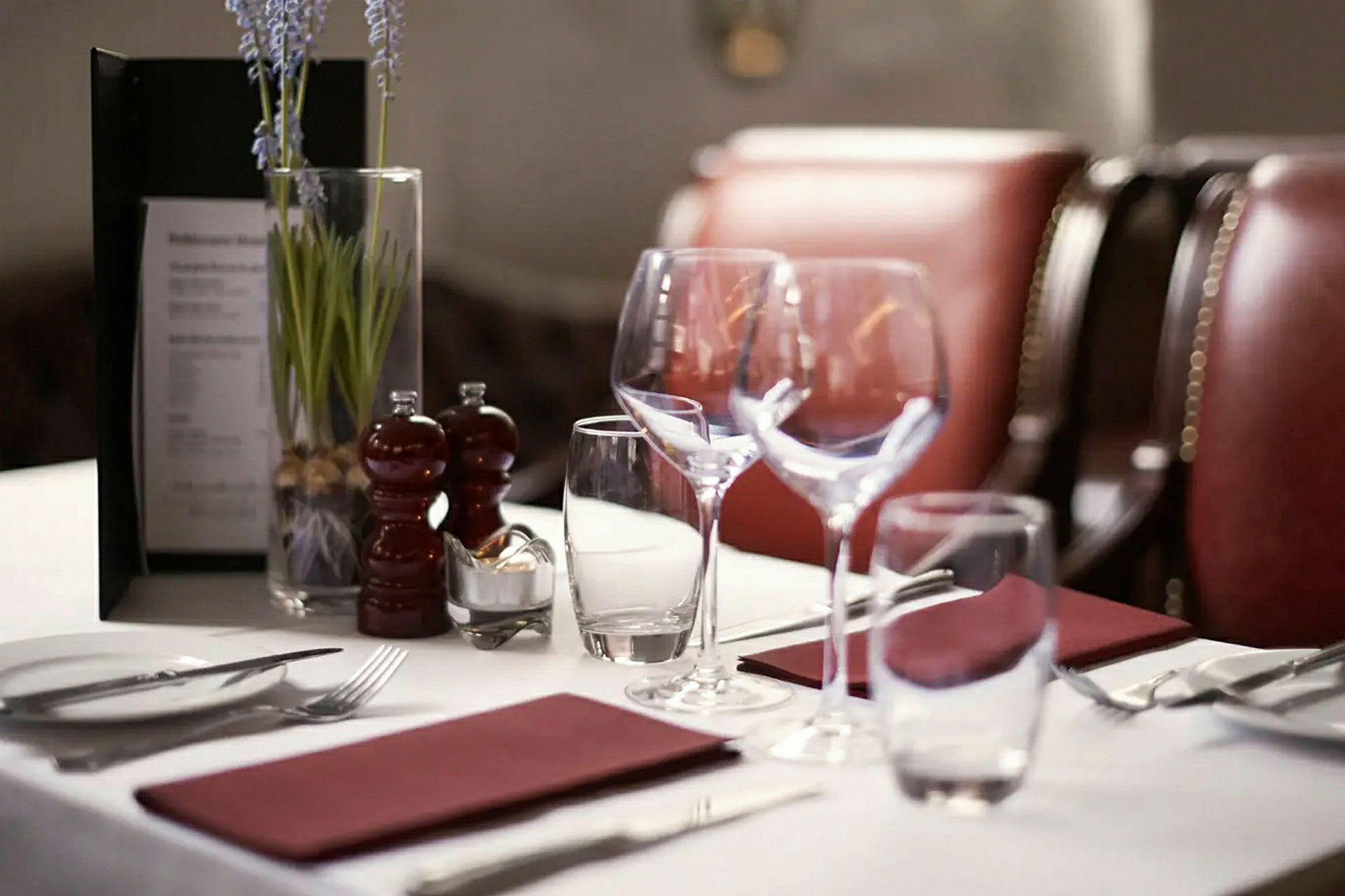 Et bord dekket med glass, bestikk, servietter og en vase med blomster på en restaurant. (AI-generert tekst)
