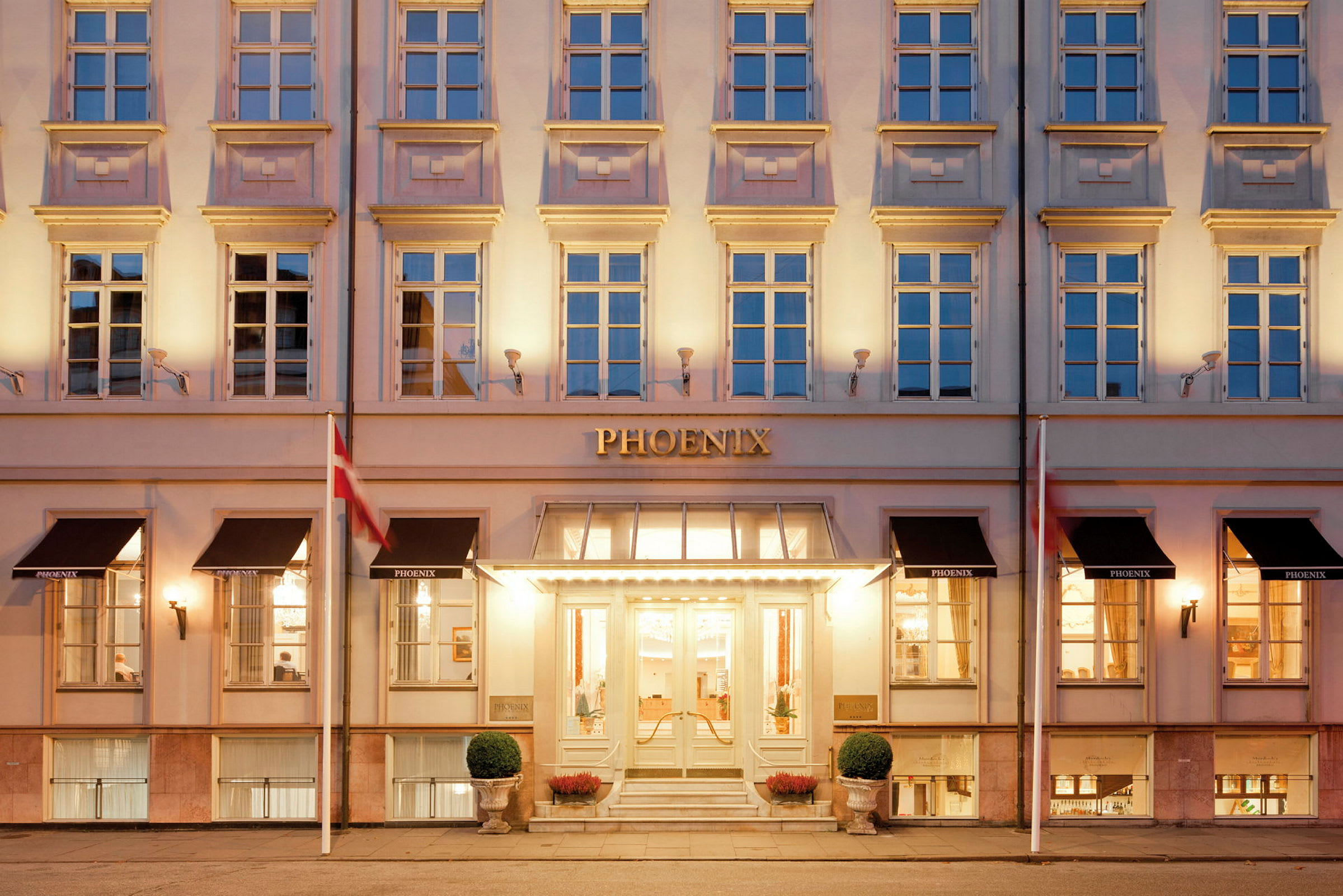 Bildet viser en eksteriør av et hotell med en opplyst inngang og klassisk fasade. (AI-generert tekst)