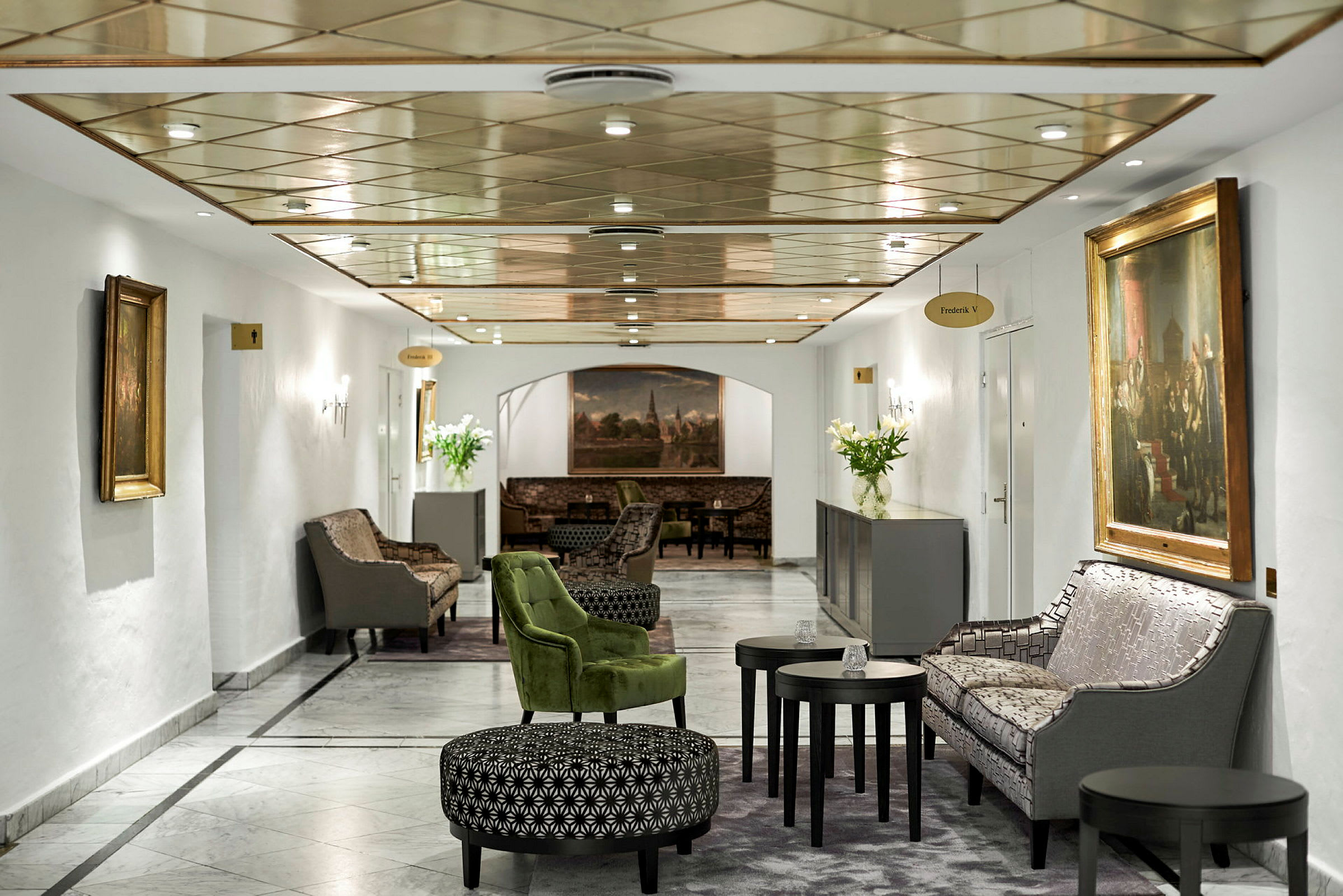 Et smakfullt innredet loungeområde med sofaer, stoler og bord, omgitt av malerier og dekorative detaljer. (AI-generert tekst)