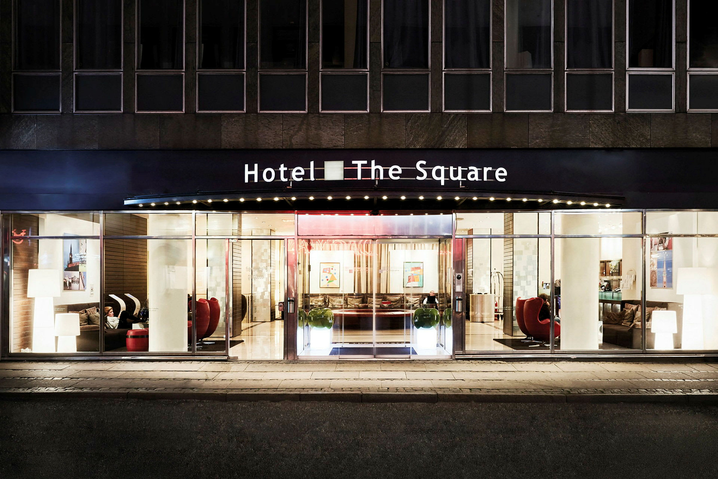 Inngangen til et hotell med navnet "The Square" opplyst om kvelden. (AI-generert tekst)