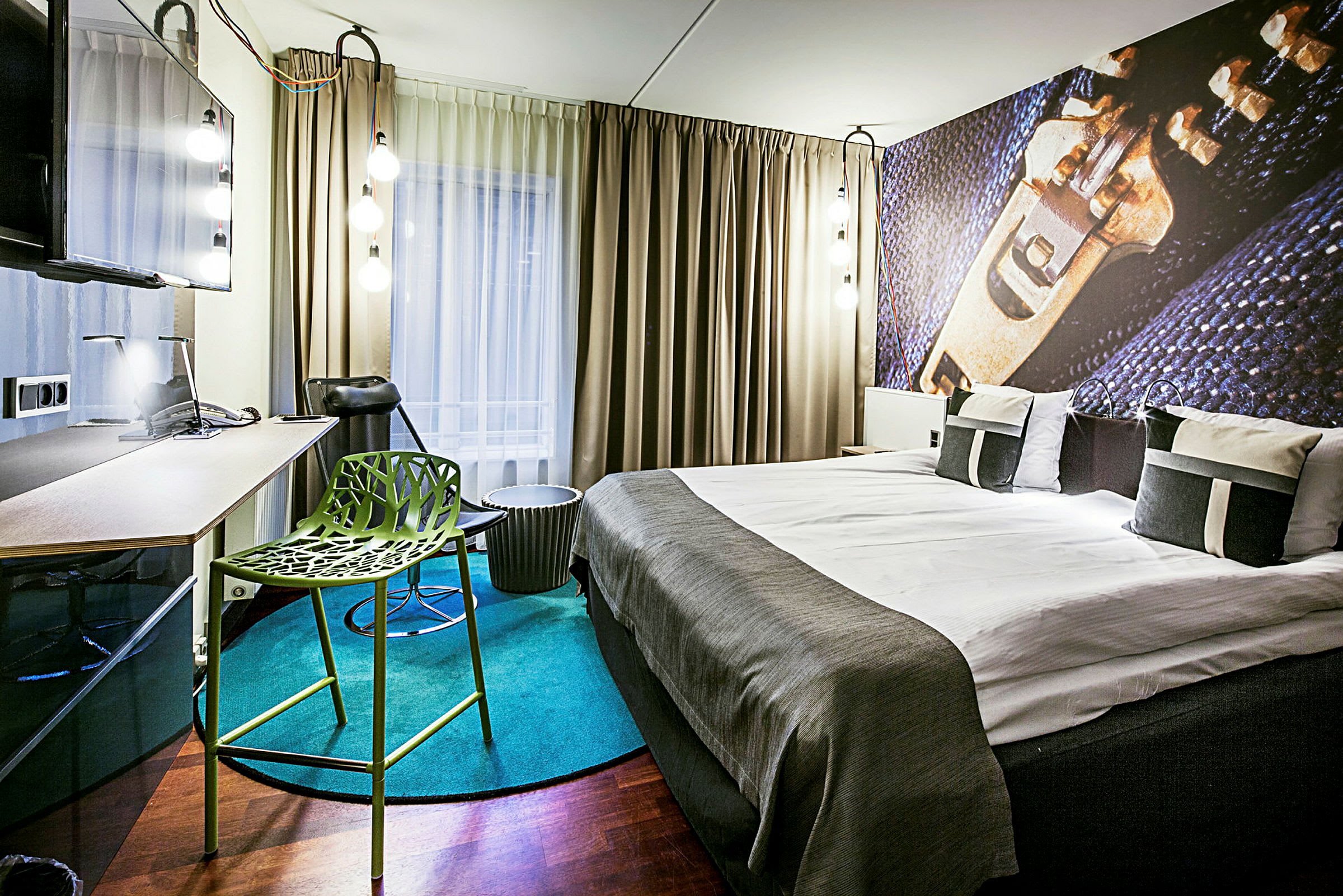 Et moderne innredet hotellrom med en dobbeltseng, skrivebord, grønn stol og store gardiner foran vinduet. (AI-generert tekst)