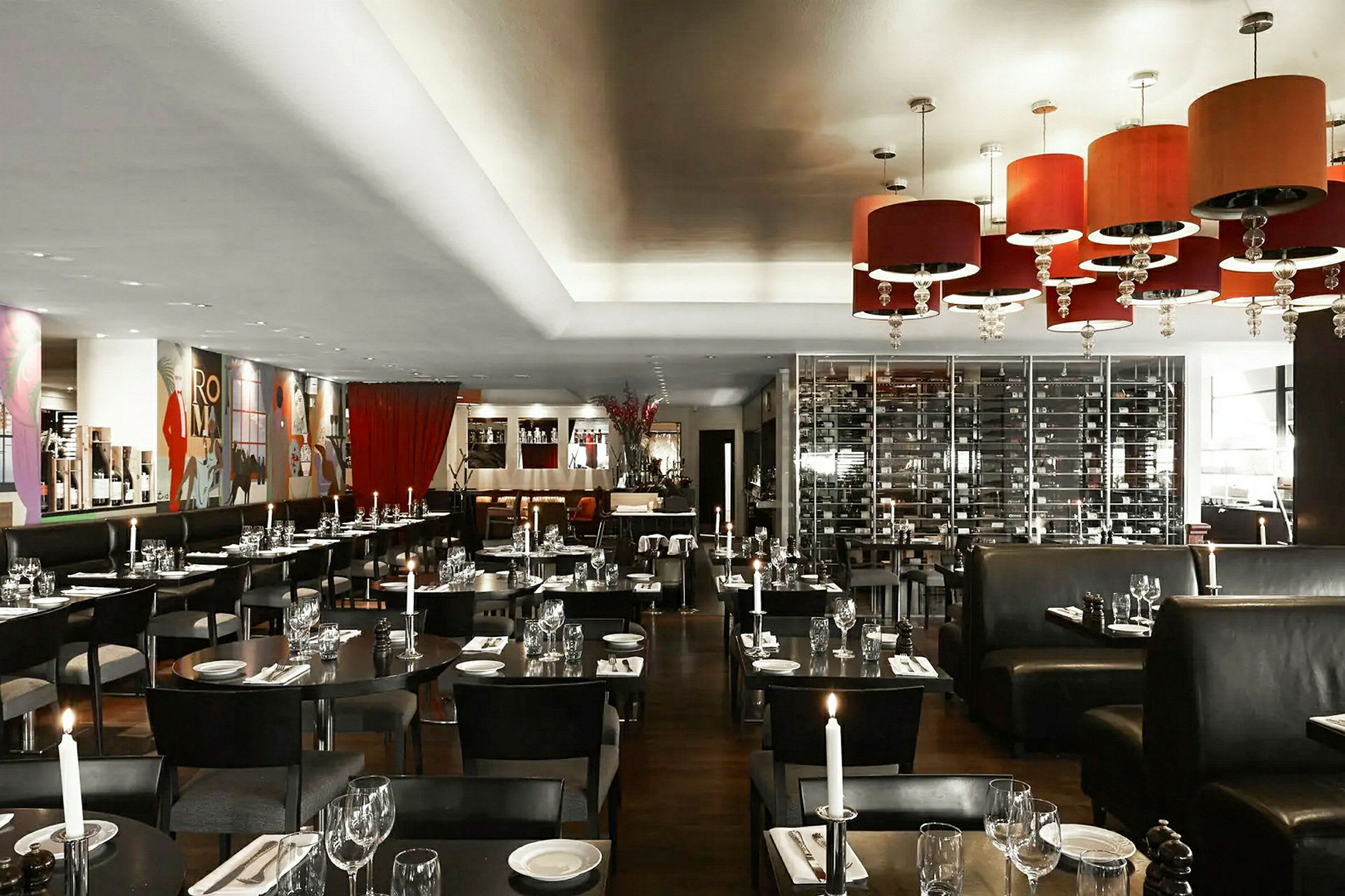 En elegant innredet restaurant med tente lys, mørke møbler og et hengende vinkjeller som bakgrunn. (AI-generert tekst)