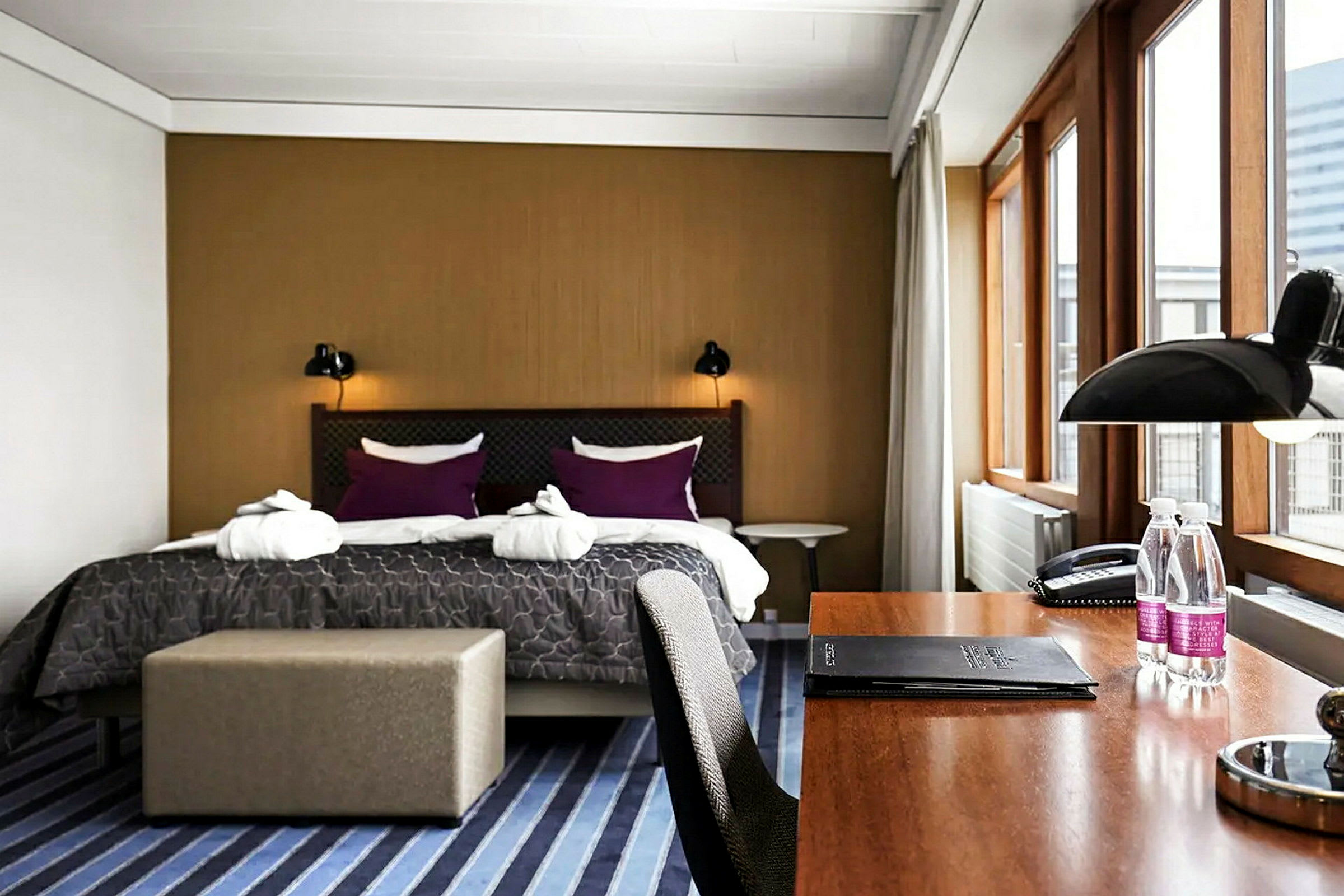 Et hotellrom med en stor dobbeltseng, skrivebord og store vinduer. (AI-generert tekst)