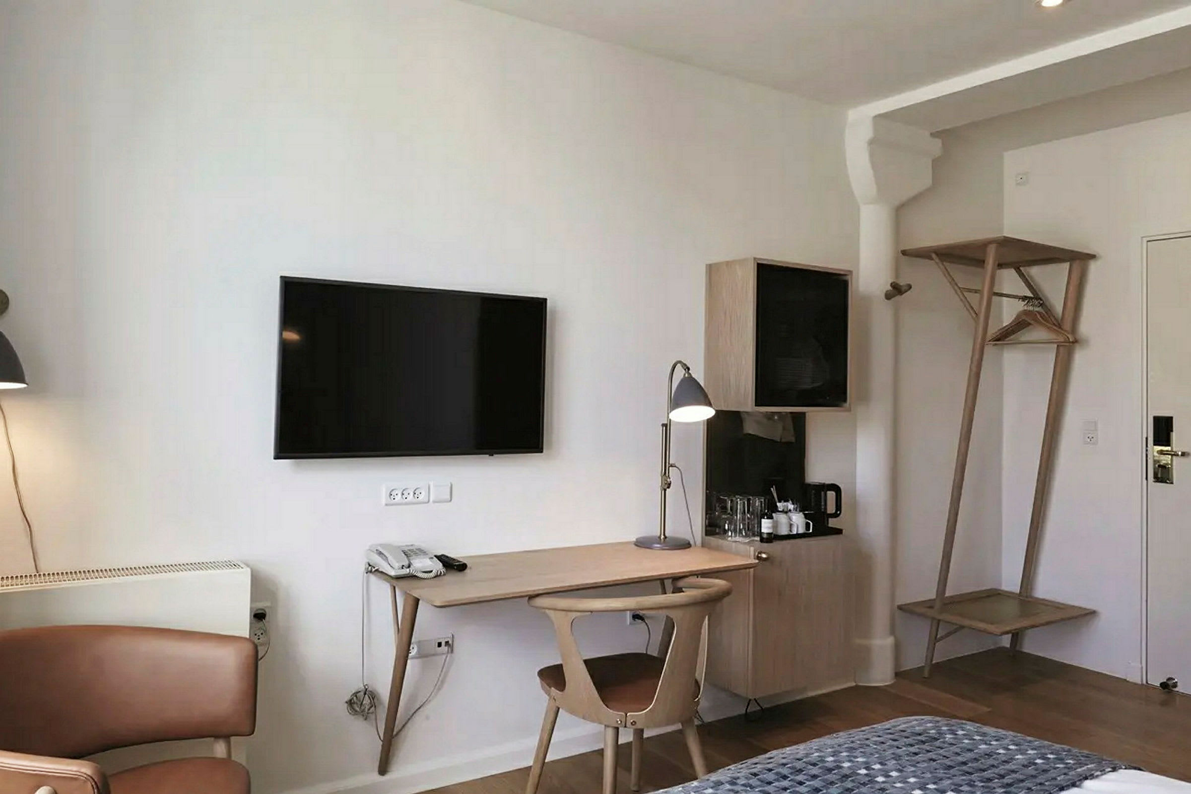 Et hotellrom med en arbeidsplass som inkluderer et skrivebord, en stol og en skrivebordslampe. En TV er montert på veggen over. (AI-generert tekst)