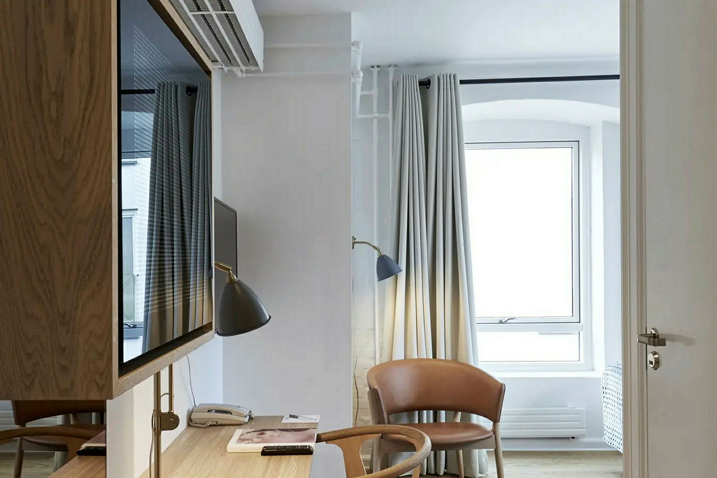 Et lyst hotellrom med skrivebord, stol og vindu. (AI-generert tekst)